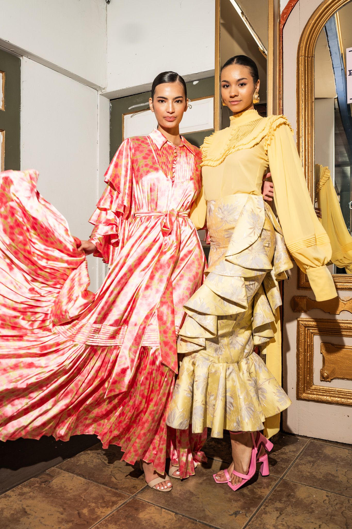 Fashion models pose in contrasting red and gold ruffled dresses against ornate mirrors.