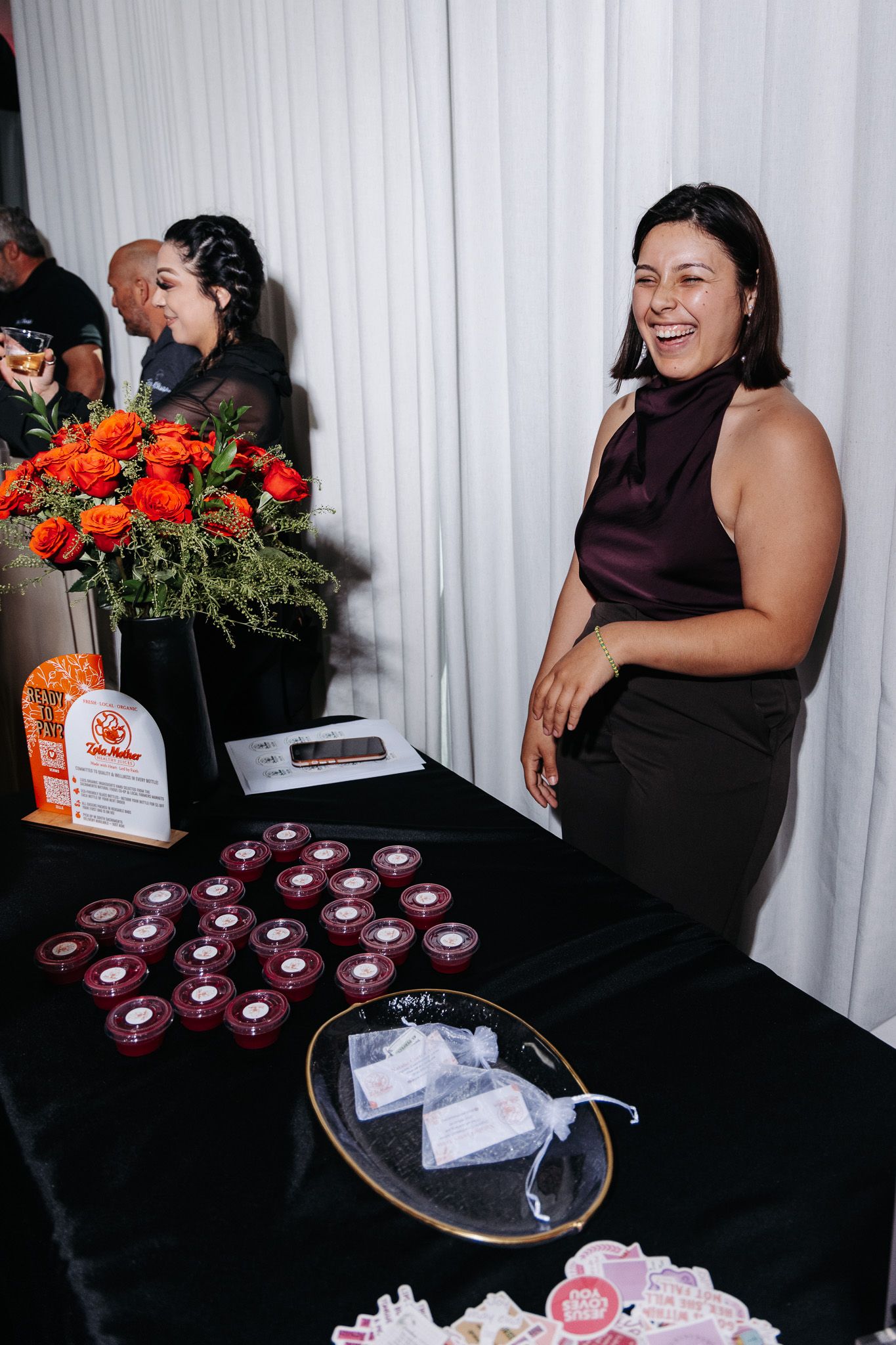 Event staff member stands at table with red floral centerpiece and drinks at catered function.