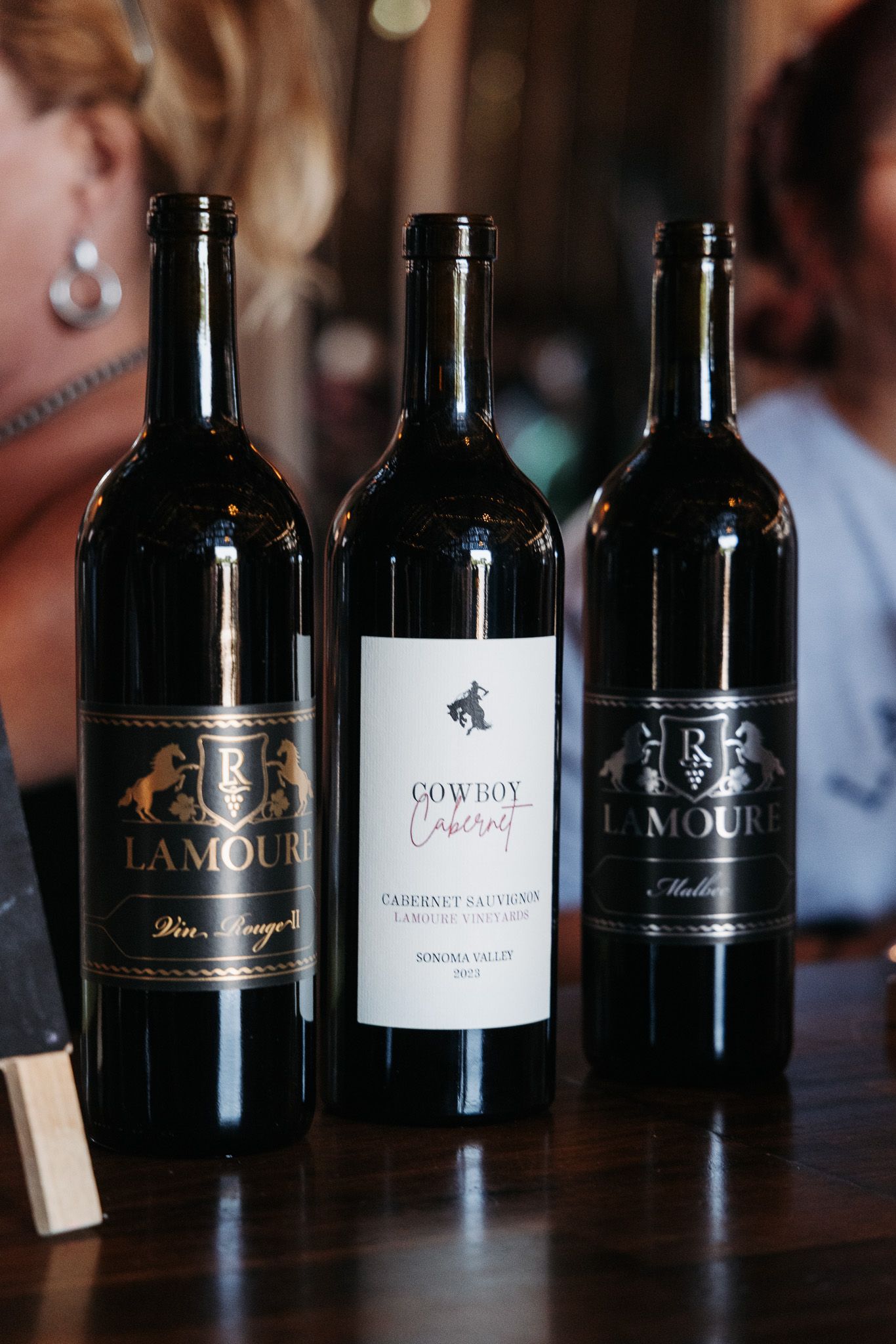 Three LaMoure Vineyard wine bottles including Cowboy Cabernet Sauvignon from Sonoma Valley displayed on a wooden surface.