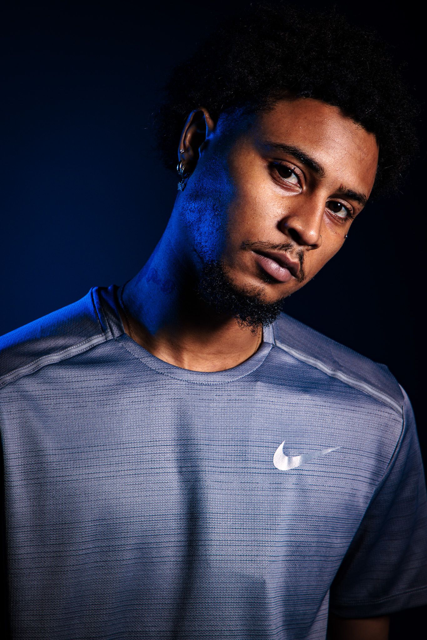 Young man in Nike athletic shirt posed against dark blue background with studio lighting.