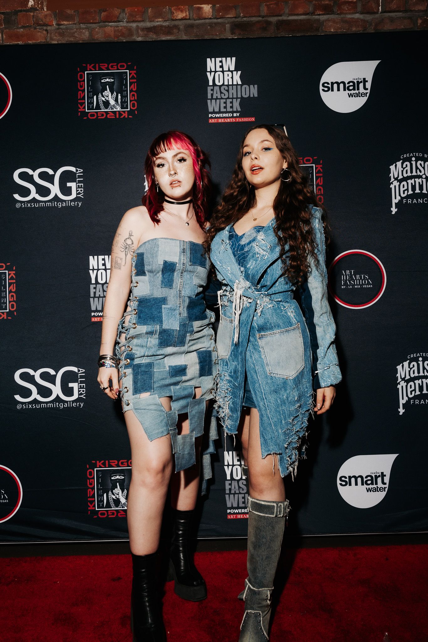 Two models showcase denim-inspired outfits on the red carpet at a fashion event.