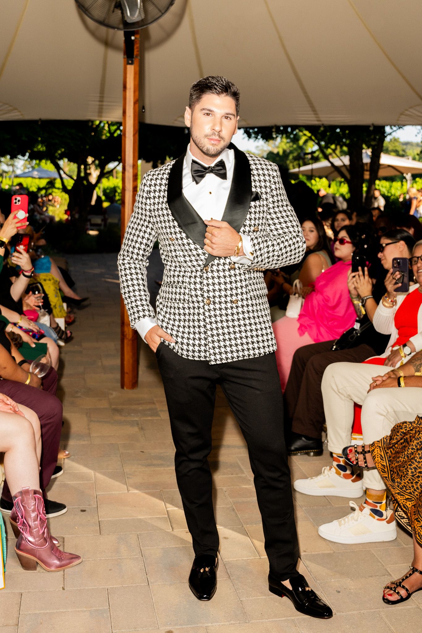 A performer in a black and white houndstooth suit and bowtie entertains guests at an outdoor event under a tent.