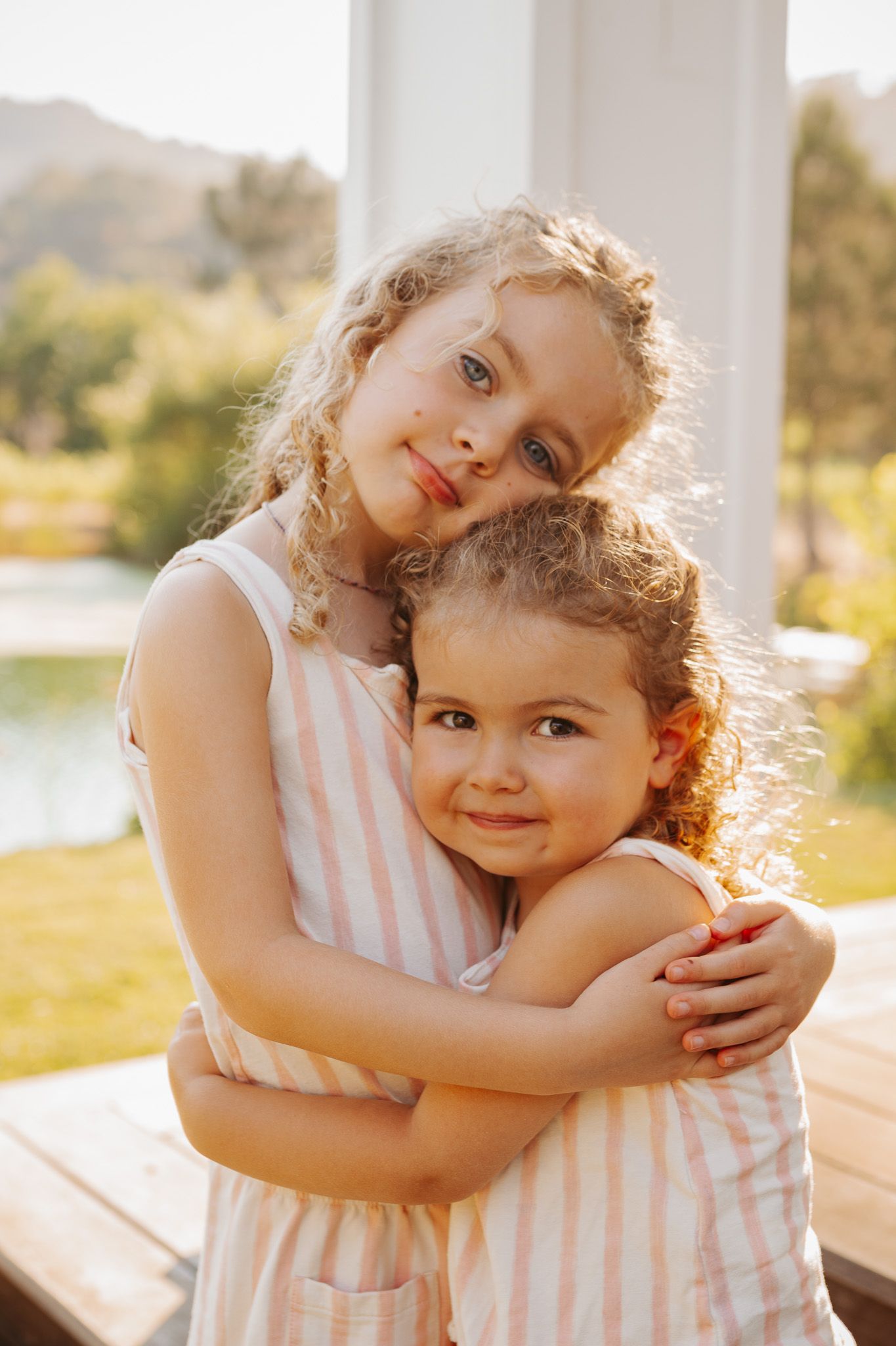 Two children in matching striped outfits share sweet embraces in a series of warm, sunlit outdoor portraits.