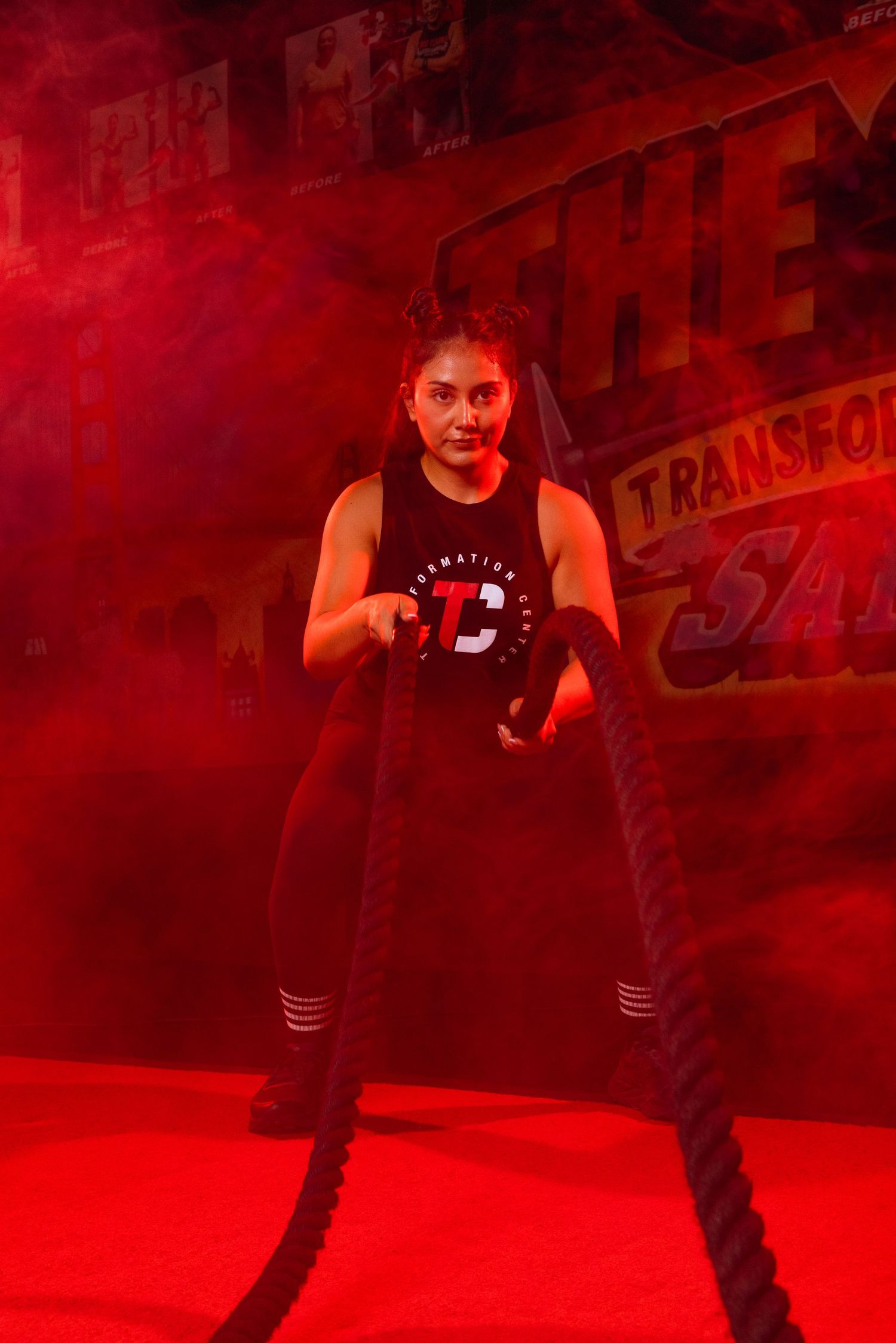 Athletic figure in black workout attire performs dynamic exercise in red-lit fitness studio setting.