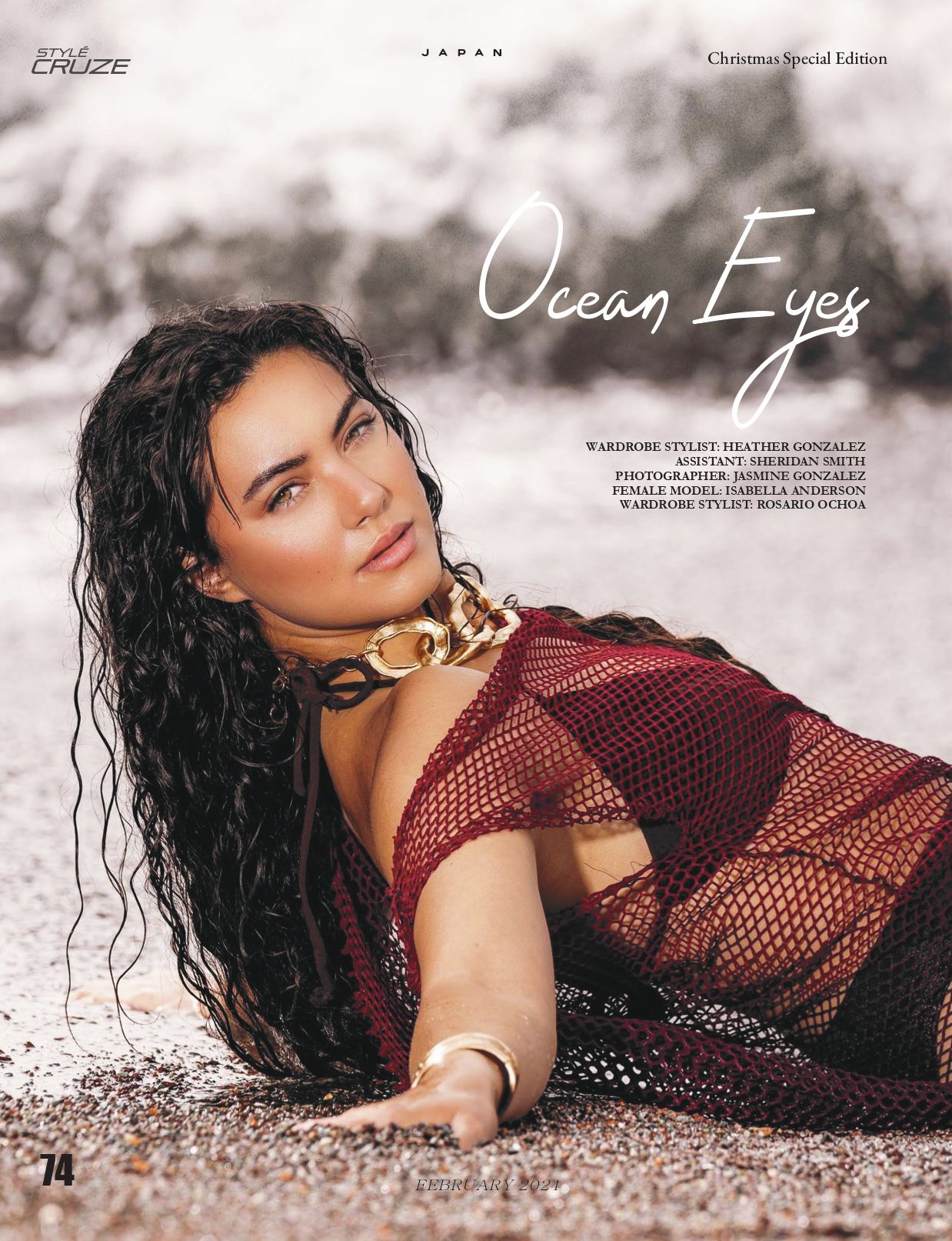 Fashion portrait of model in burgundy mesh dress lying on sand with wet hair.