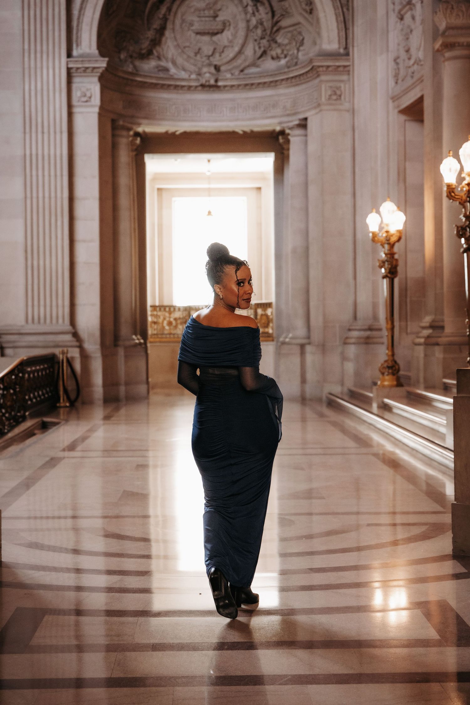 Four sequential frames show a person in a dark dress walking through an ornate marble hallway with classical architecture.