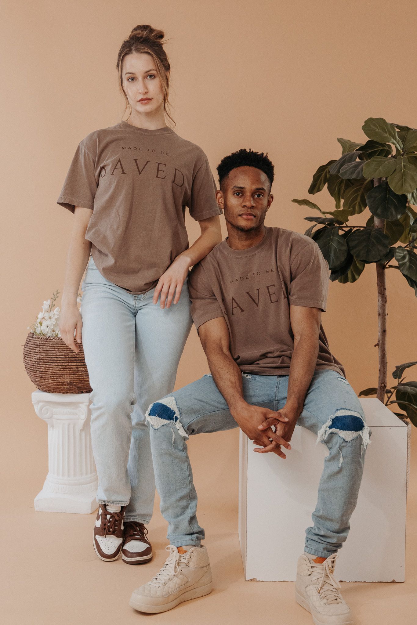 Two people in matching brown sweatshirts and light denim jeans pose together against a beige backdrop.