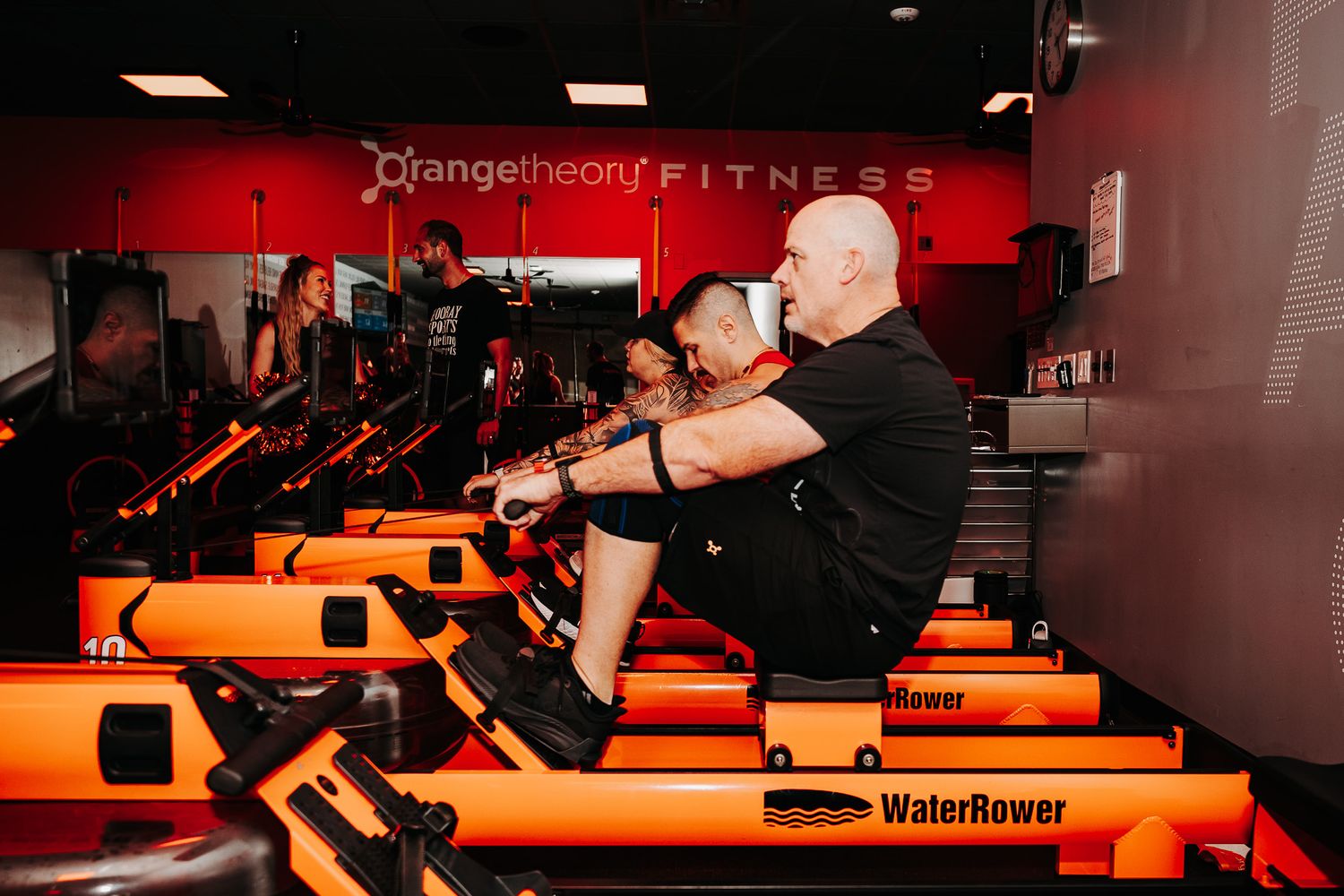 Orange and black fitness studio with exercise equipment and groups training under red lights.