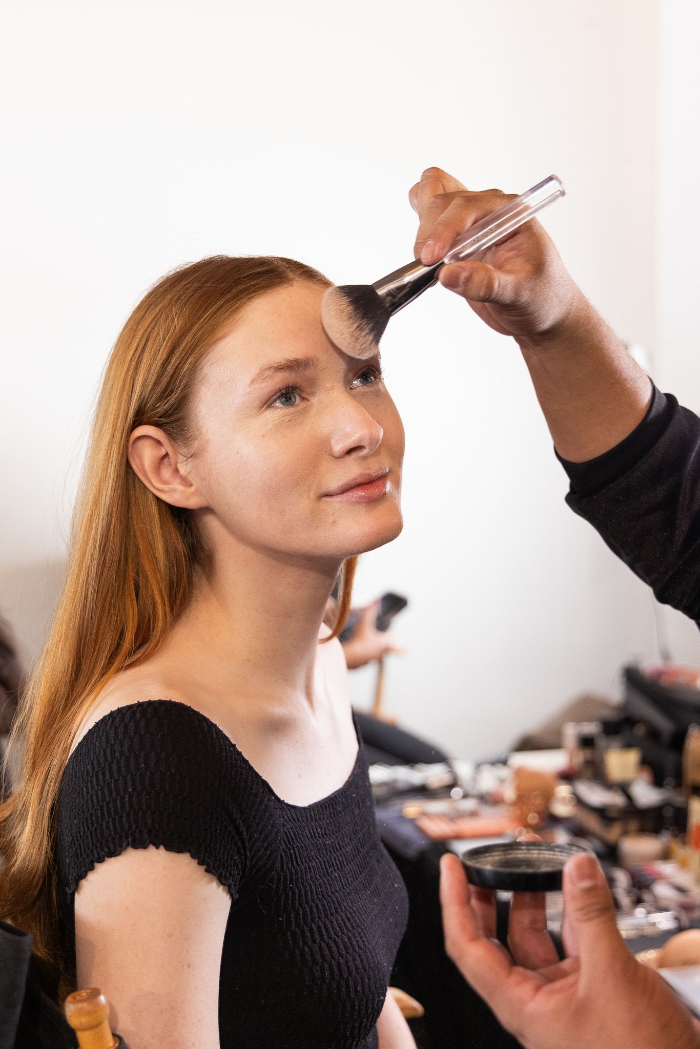 Professional makeup artist applying cosmetics with brushes in natural light against white background during beauty session.