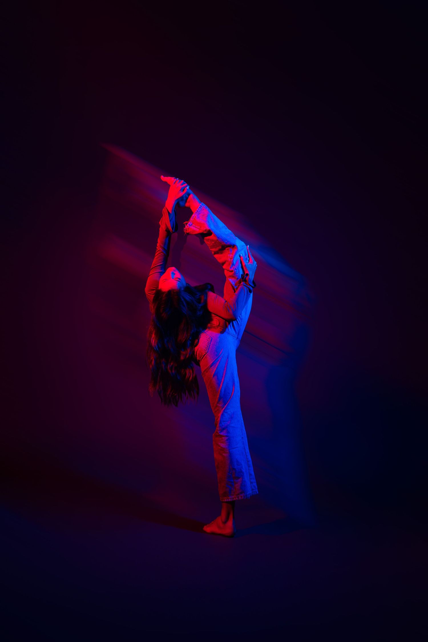 Silhouette of a person dancing in dynamic motion with dramatic red and blue lighting against a dark background.