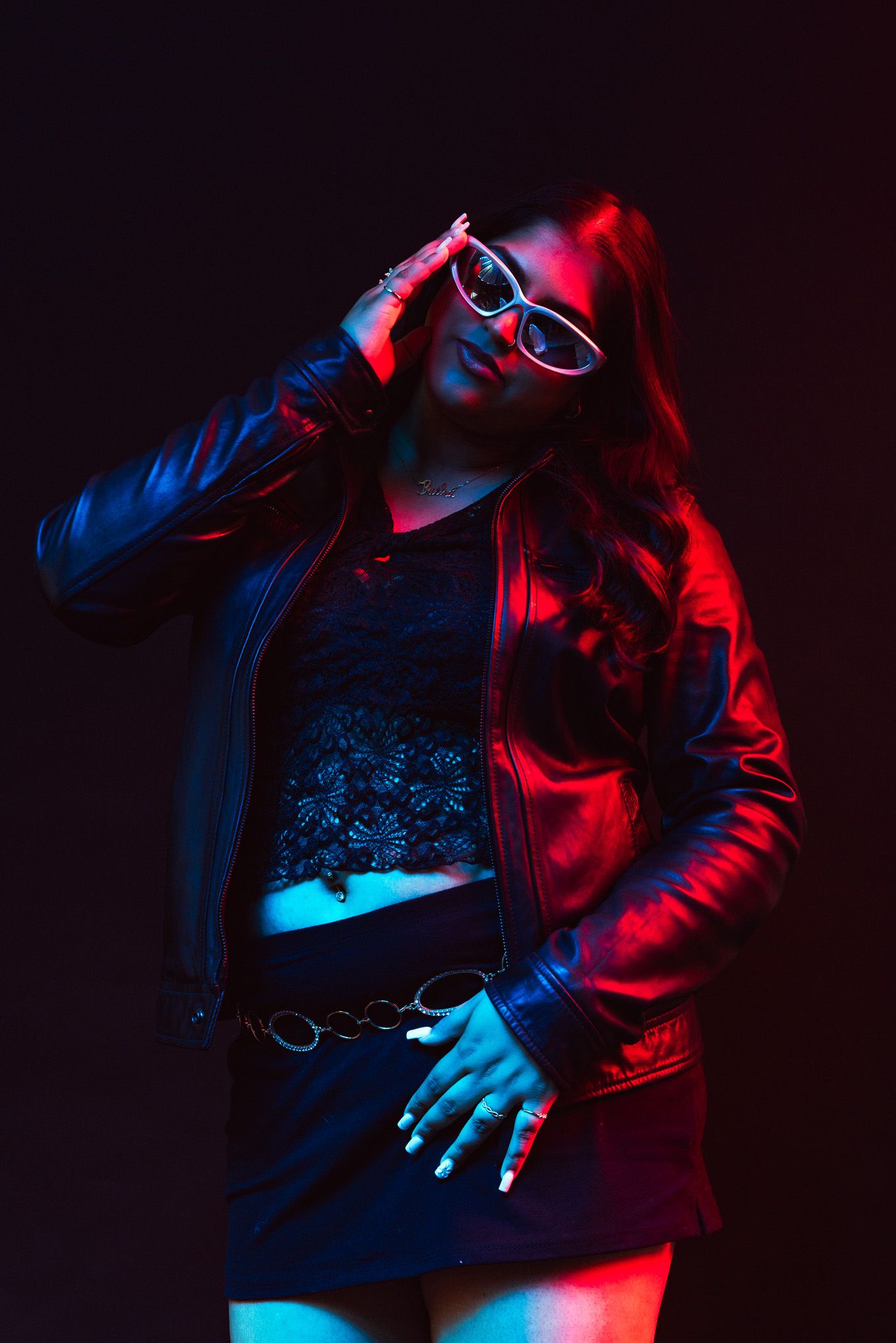 Person in dark room illuminated by dramatic red and blue lighting holds electronic device in artistic photoshoot.
