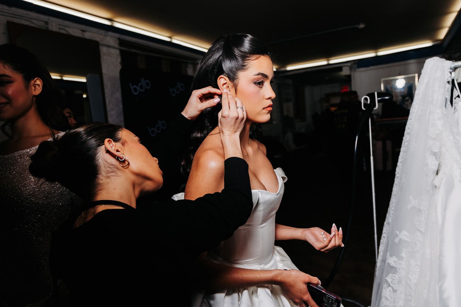 Behind-the-scenes photoshoot moments showing white gown preparations in dim studio lighting.