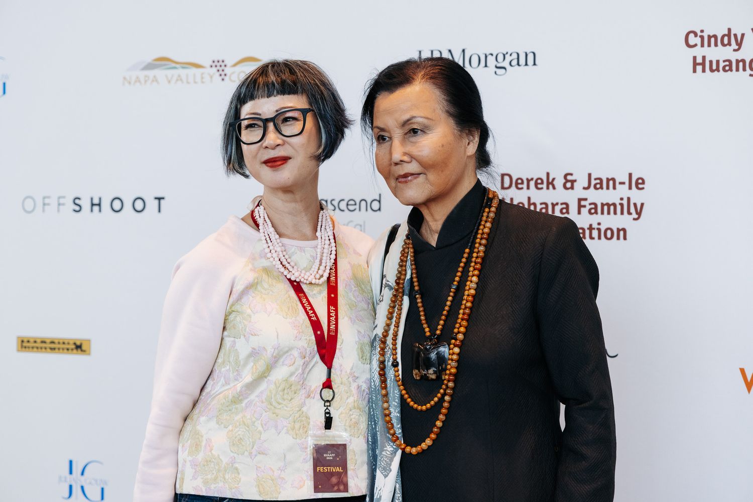 Two people wearing formal attire pose together at an event with a backdrop featuring text and logos.