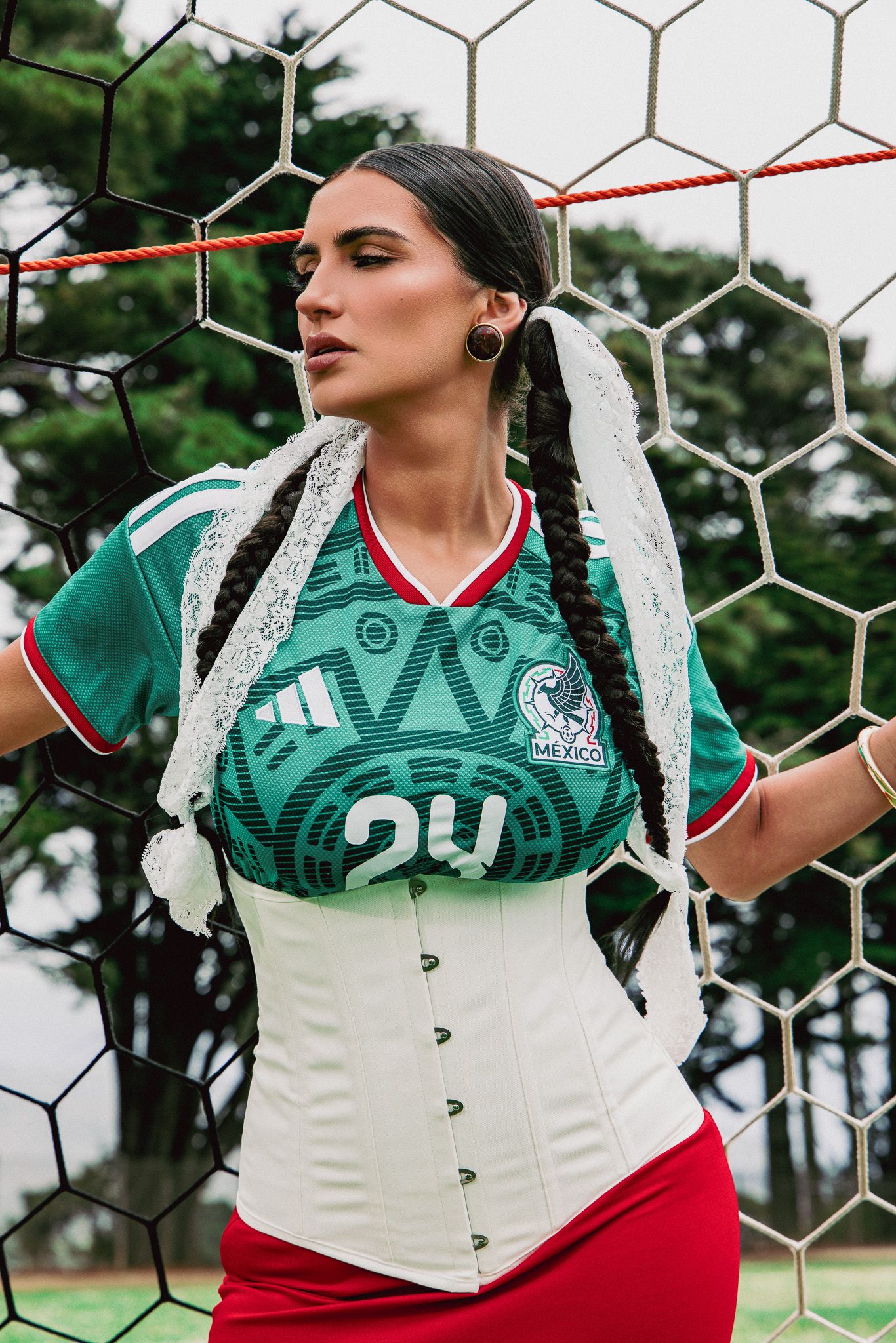 Woman in Mexico soccer jersey and white corset poses against a football goal net outdoors.