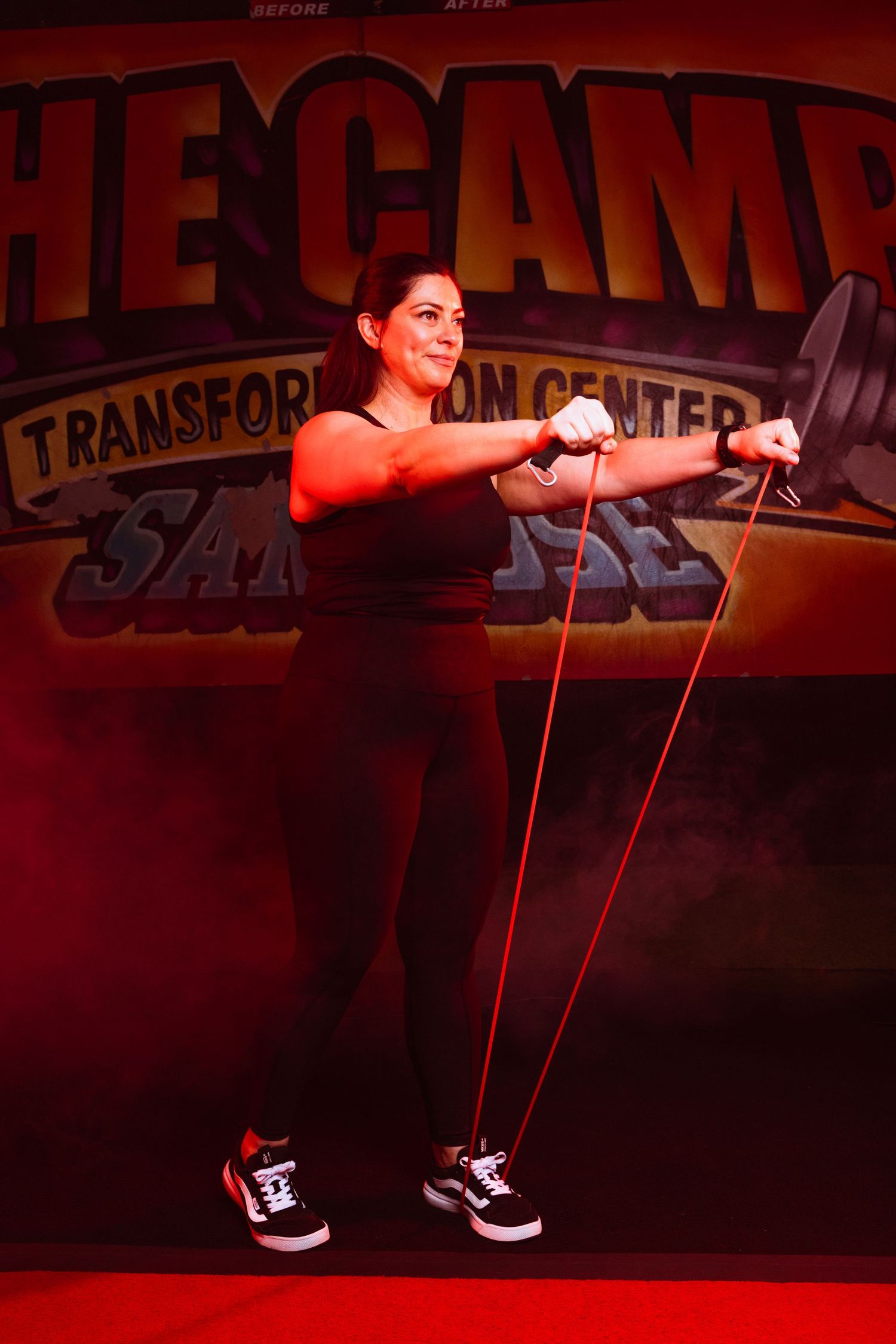 Person exercising with resistance bands in a dark gym space with red ambient lighting.
