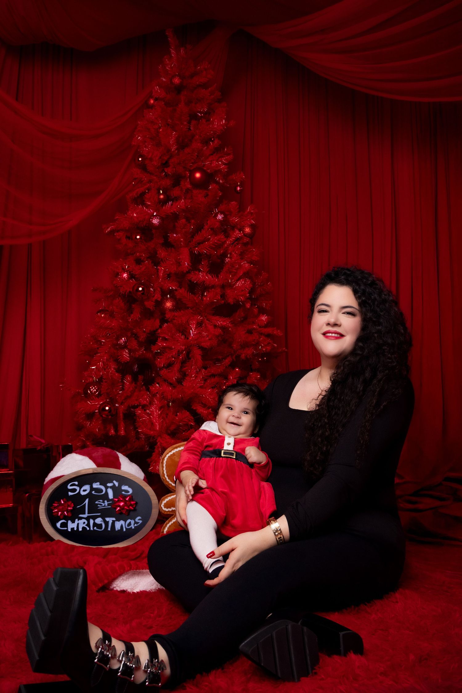 A festive holiday photo session with red curtain backdrop and Santa Christmas decorations in a studio setting.