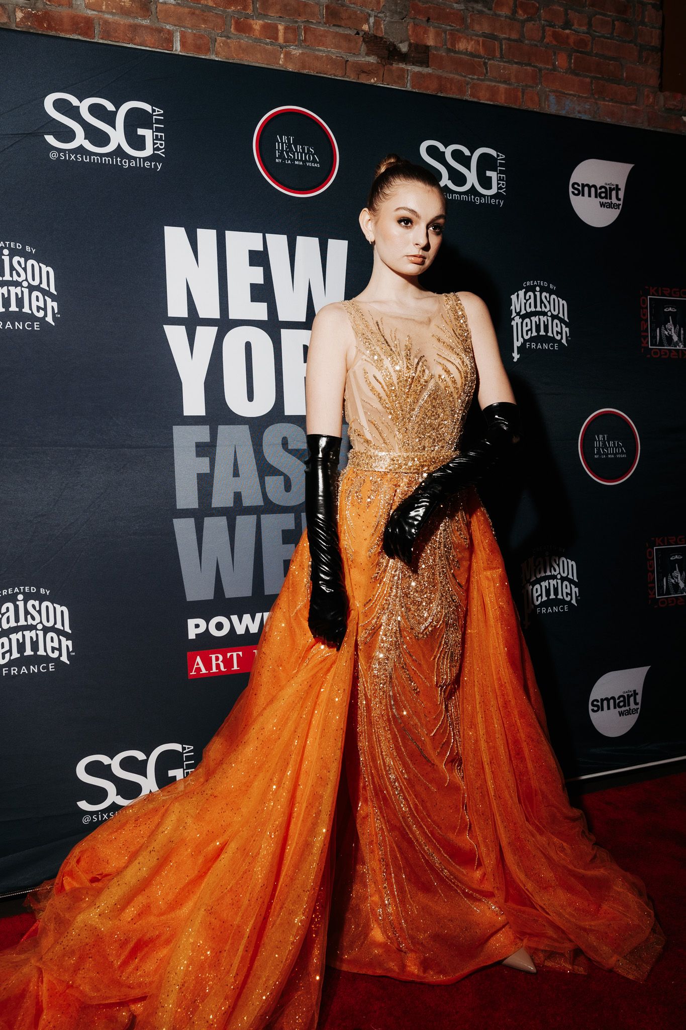 Stunning orange ballgown with glitter details photographed against New York Fashion Week backdrop.