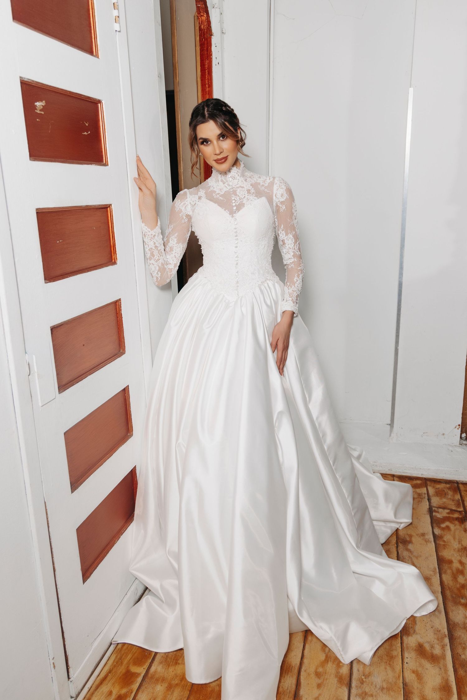 Elegant long-sleeved wedding gown with lace bodice and flowing satin skirt features high neckline and dramatic cathedral train.