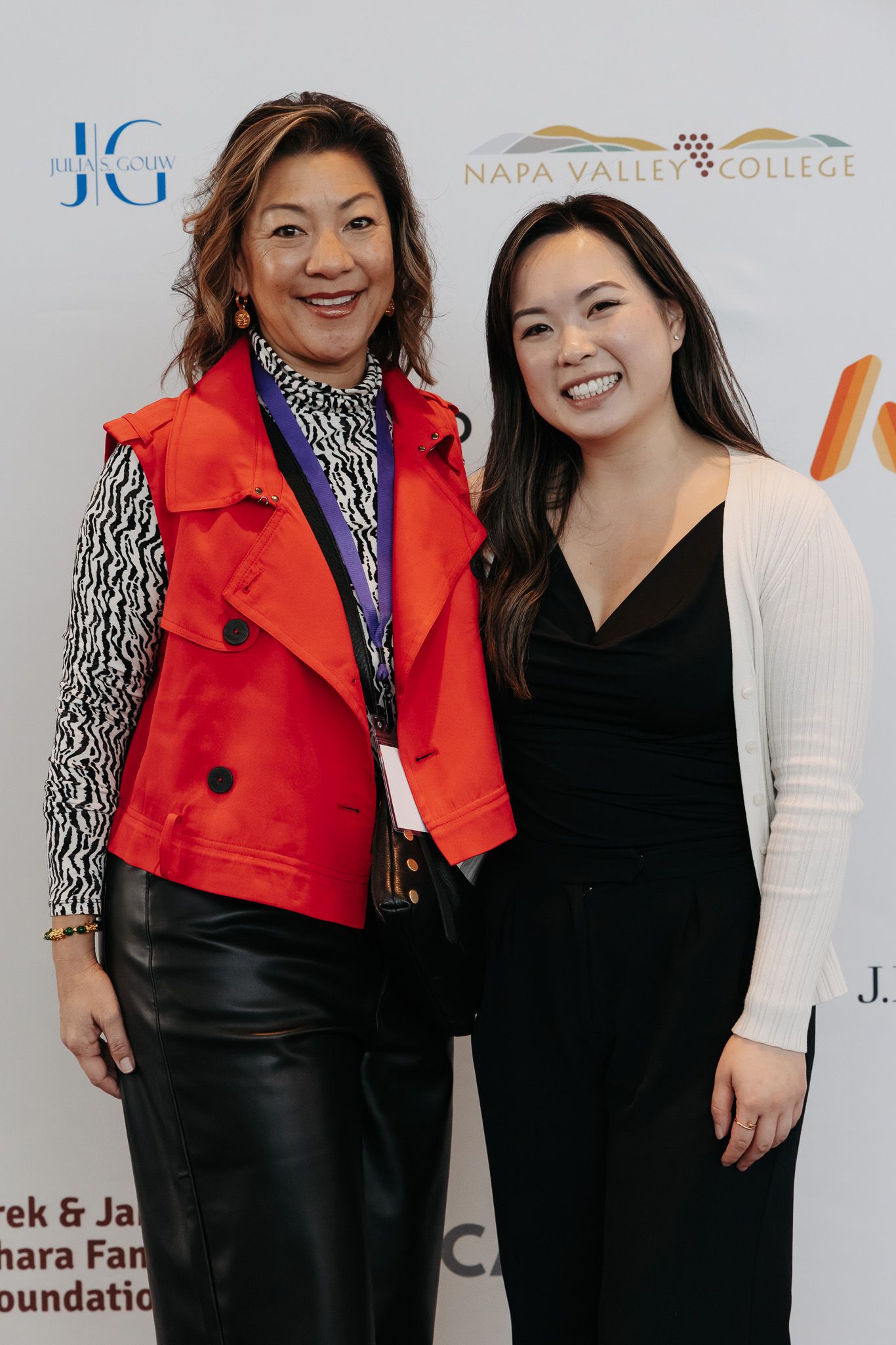 Two women pose together at an event, one wearing a striking red jacket and black and white patterned top.
