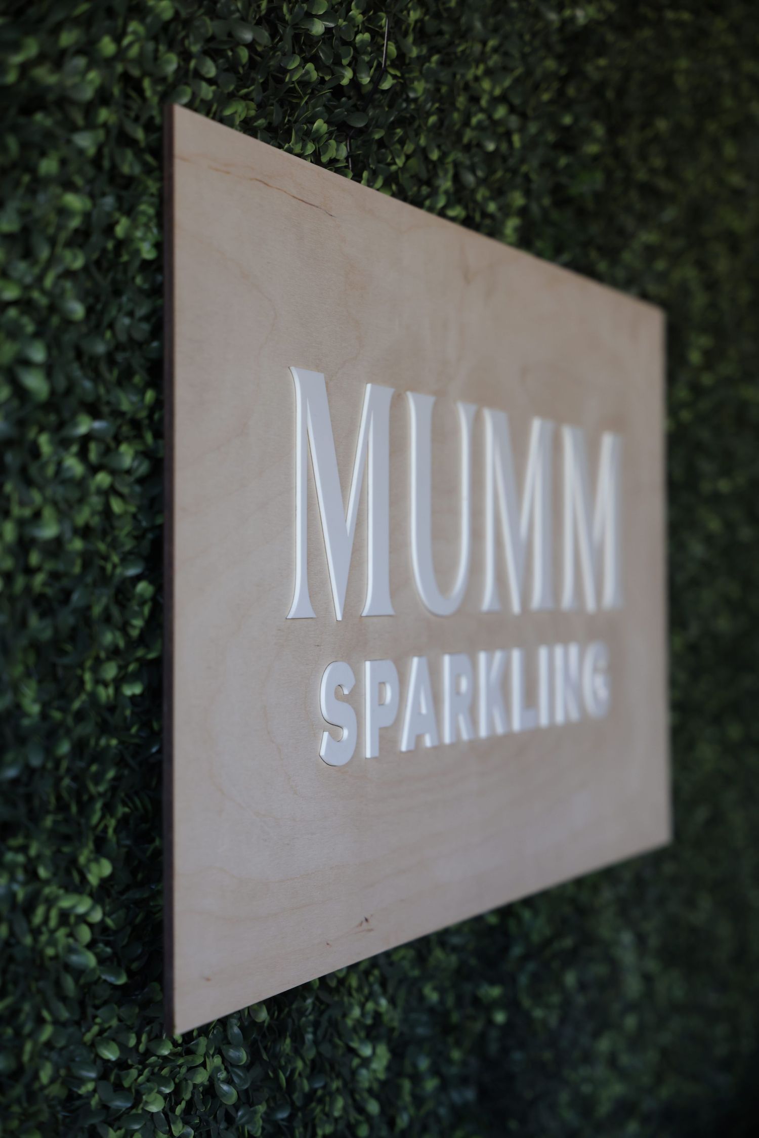 A series of five images showing a white 'MUMM SPARKLING' text sign against a dark green leafy background.
