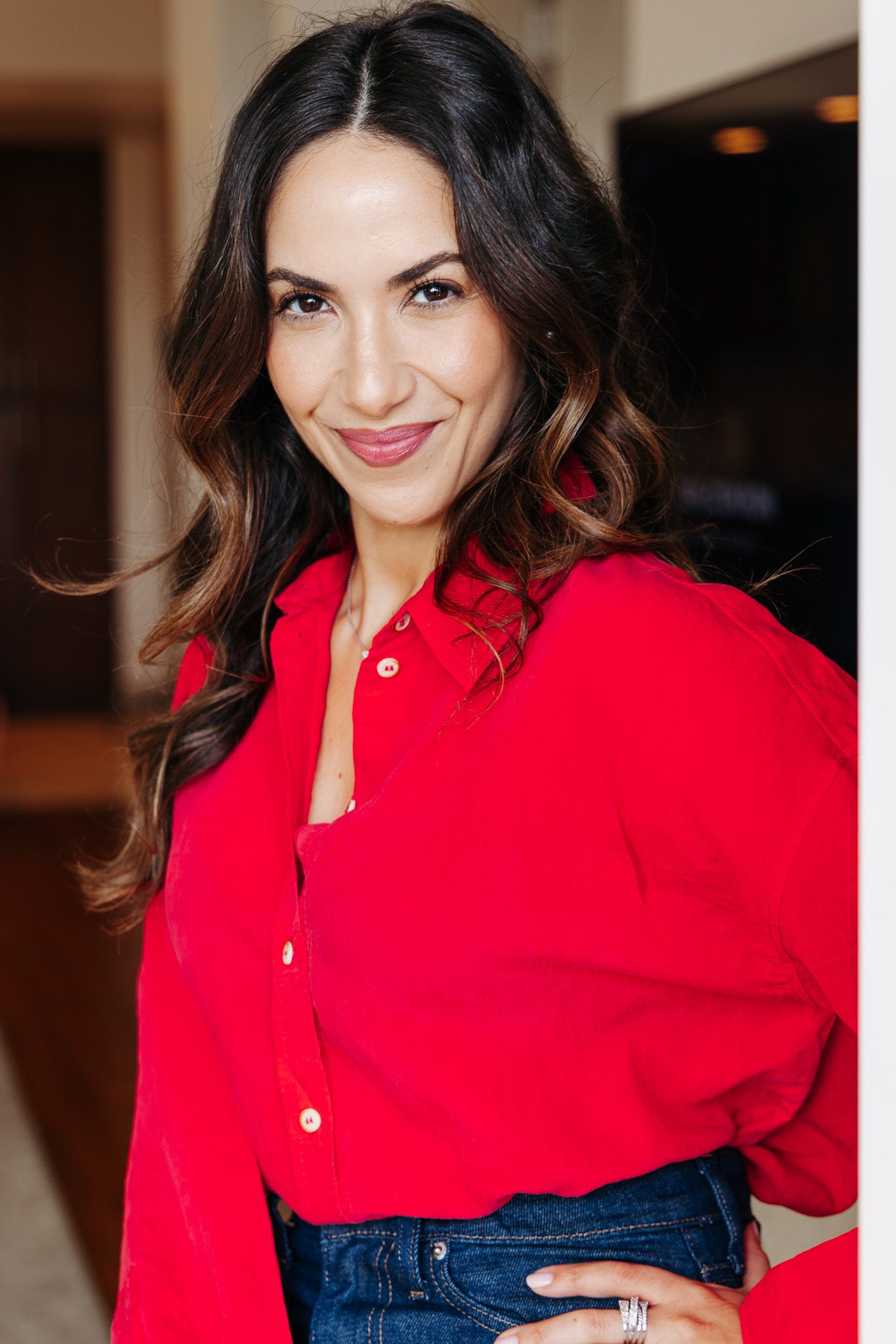 Portrait of a woman in a vibrant red blouse and jeans in an indoor setting.