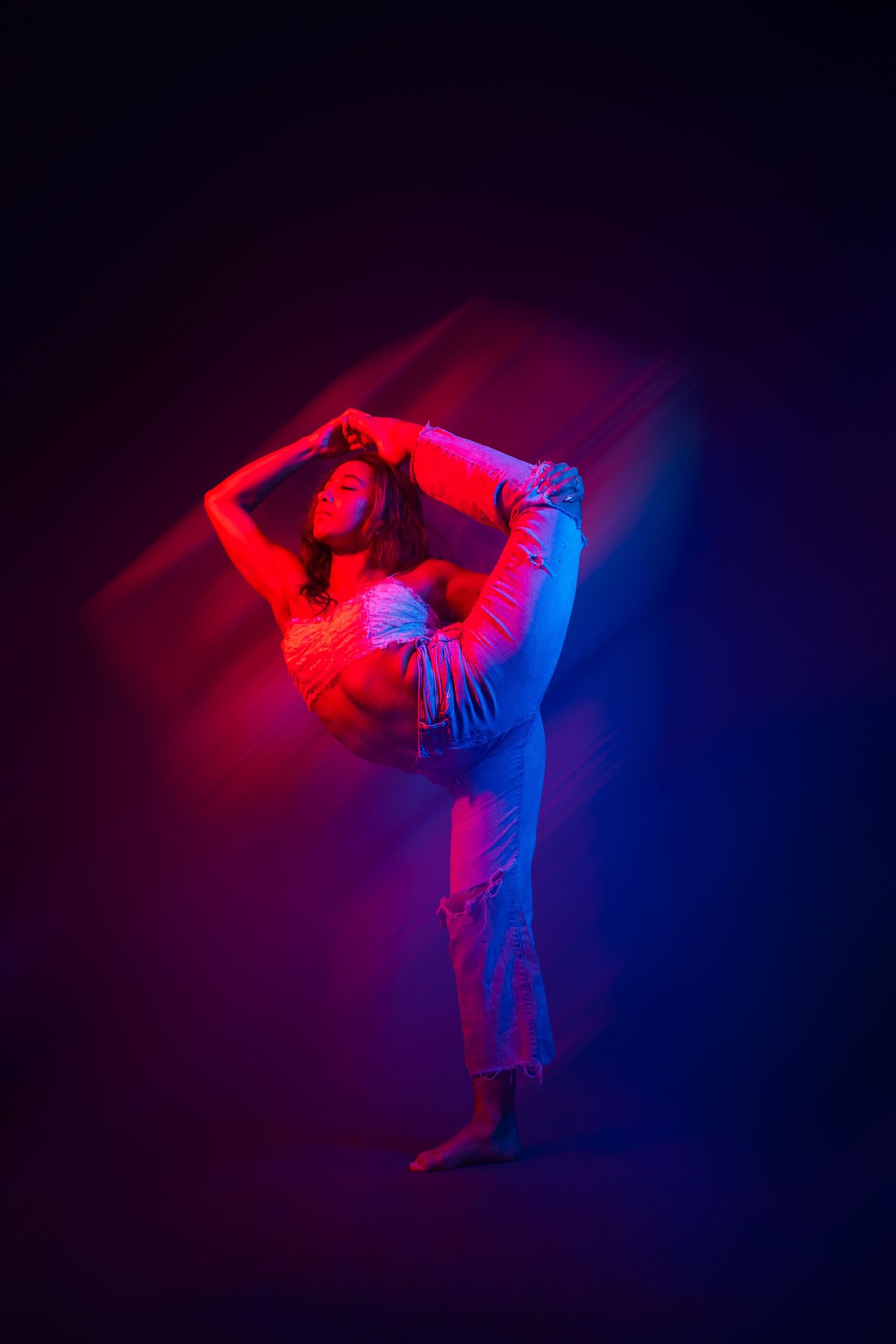A dancer performs a dynamic leap against a dark background illuminated by dramatic red and blue lighting effects.