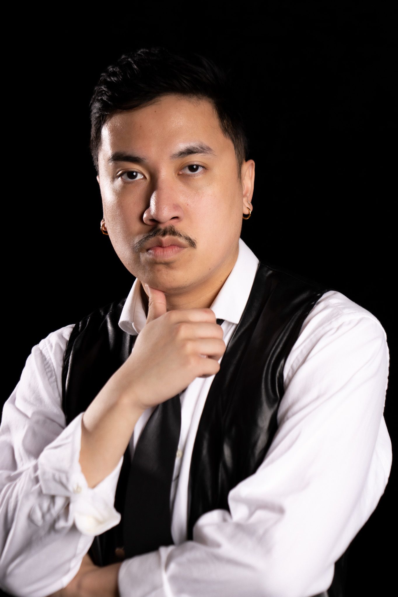 Portrait of man in white shirt and dark vest with thoughtful expression against black background.