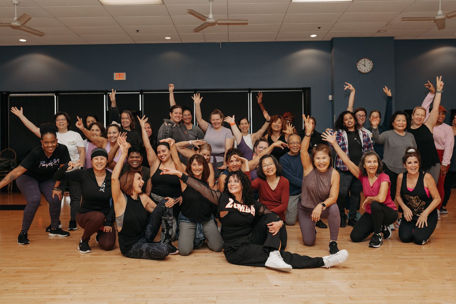 Group of dancers performing choreographed floor movements in a dance studio with wooden floors.