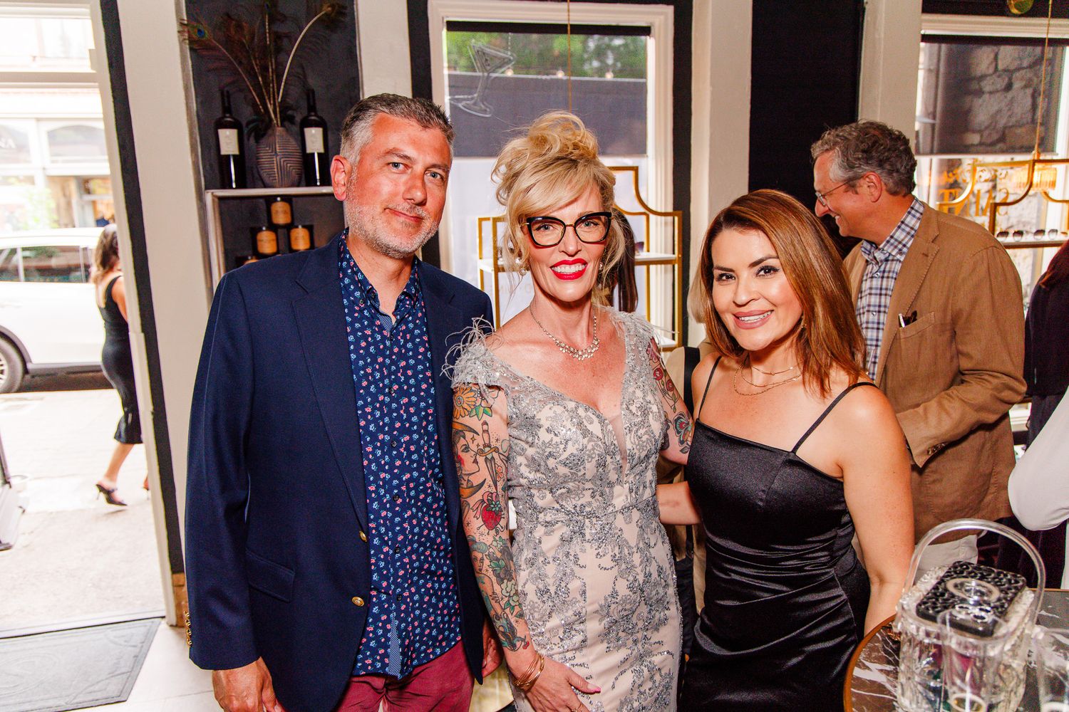 Three people posing together and smiling at an elegant indoor social event or gallery opening.