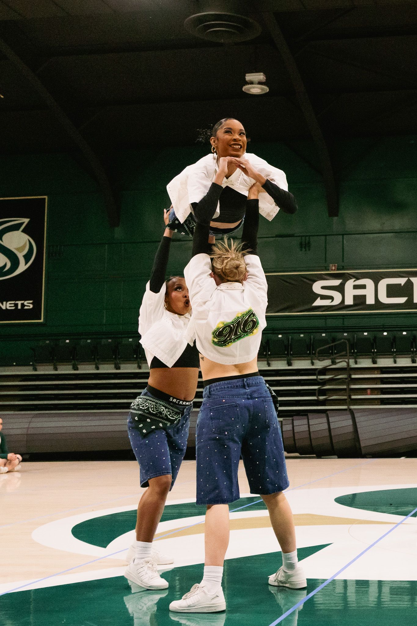 Cheerleaders performing a stunt at Sacramento State Hornets arena, with a flyer lifted by two bases on the court.