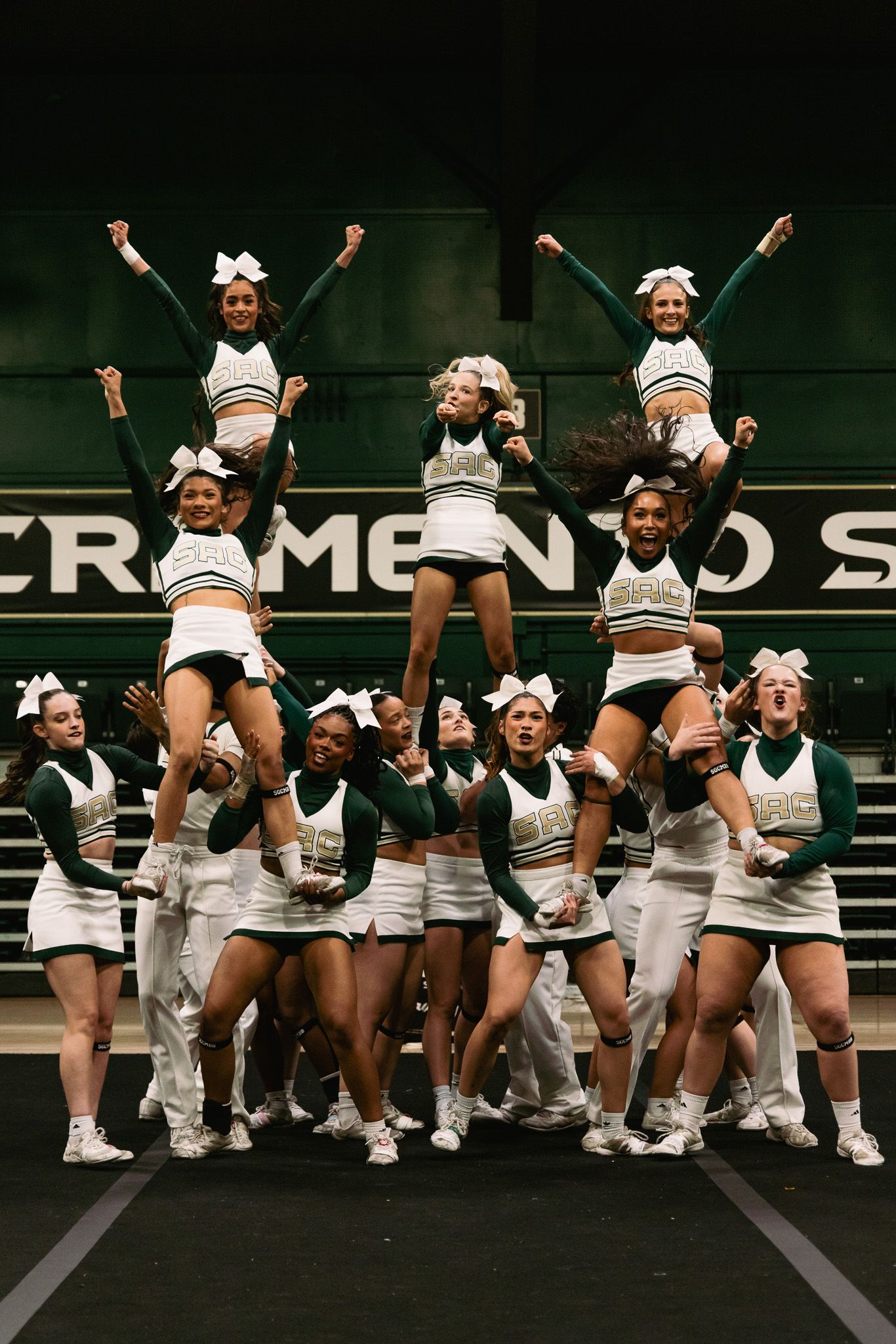 Sacramento State cheerleaders perform a pyramid stunt in green and white uniforms during a competitive cheer routine.
