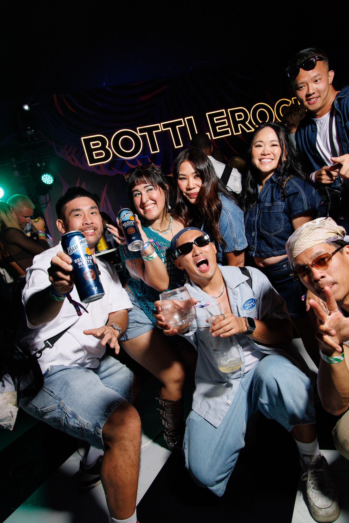 Group of friends posing and smiling at BottleRock festival, holding drinks and cans in a dark venue.