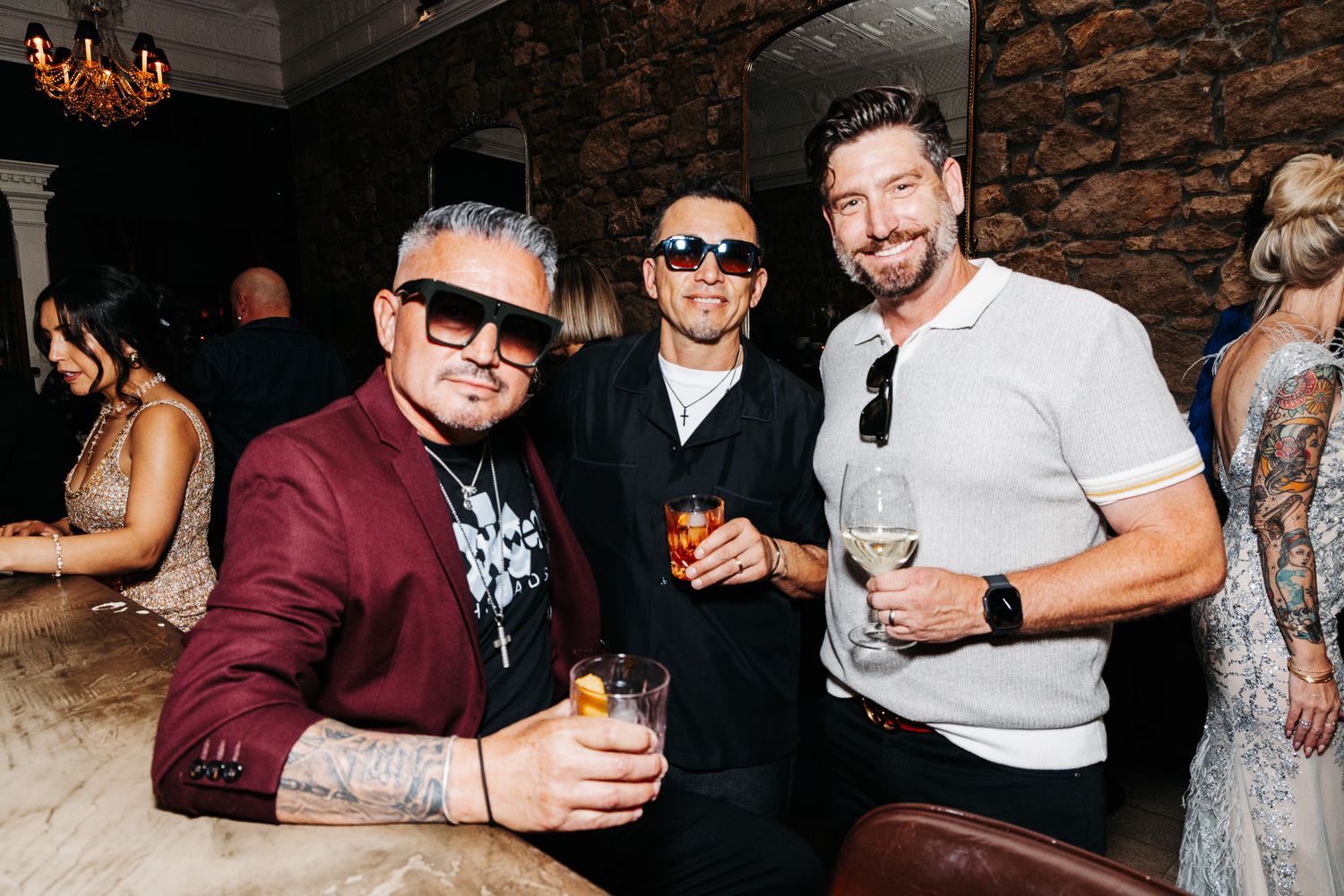 Three men smiling and holding drinks at an upscale indoor party event.