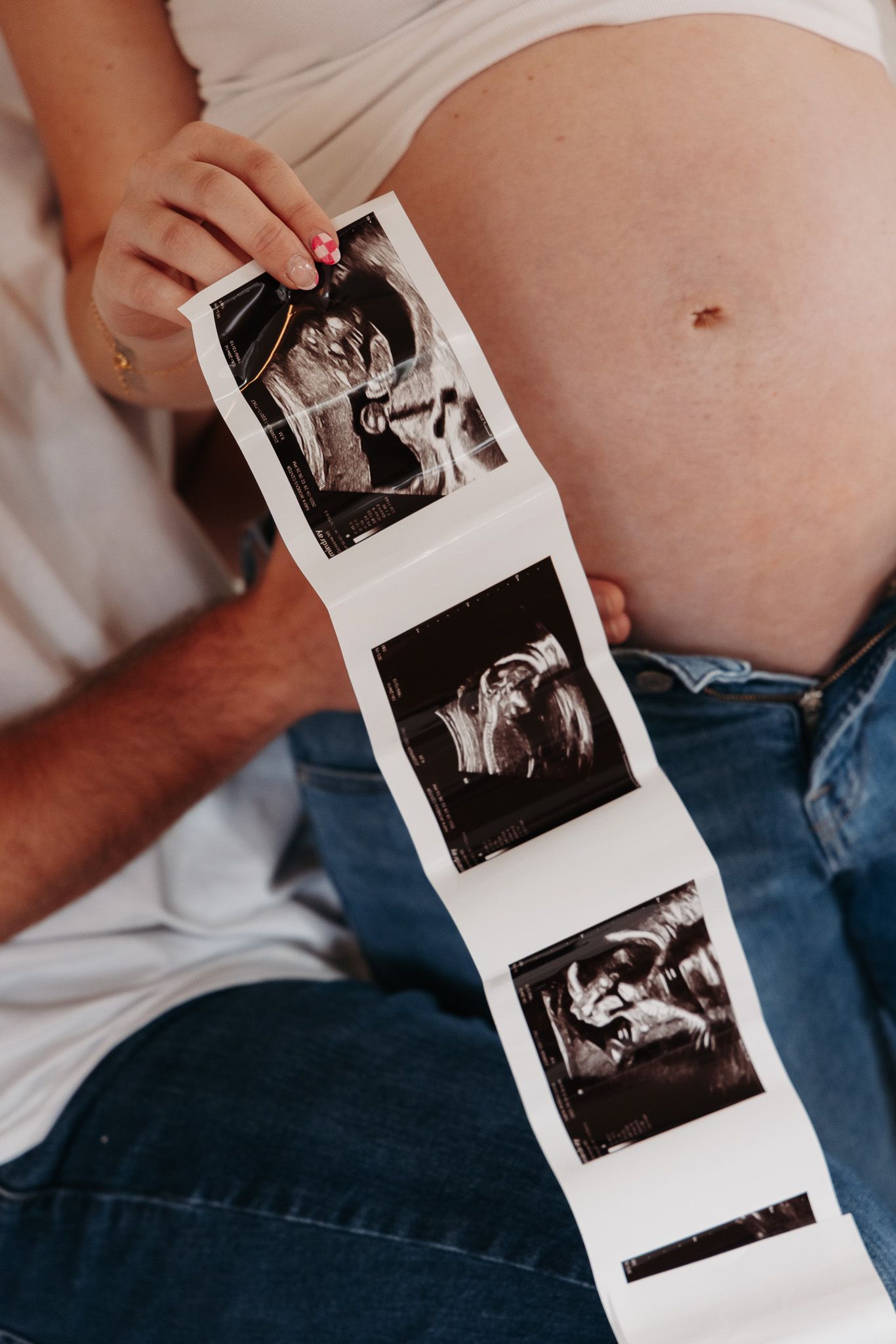 A series of black and white ultrasound photos being held against a pregnant belly wearing jeans.