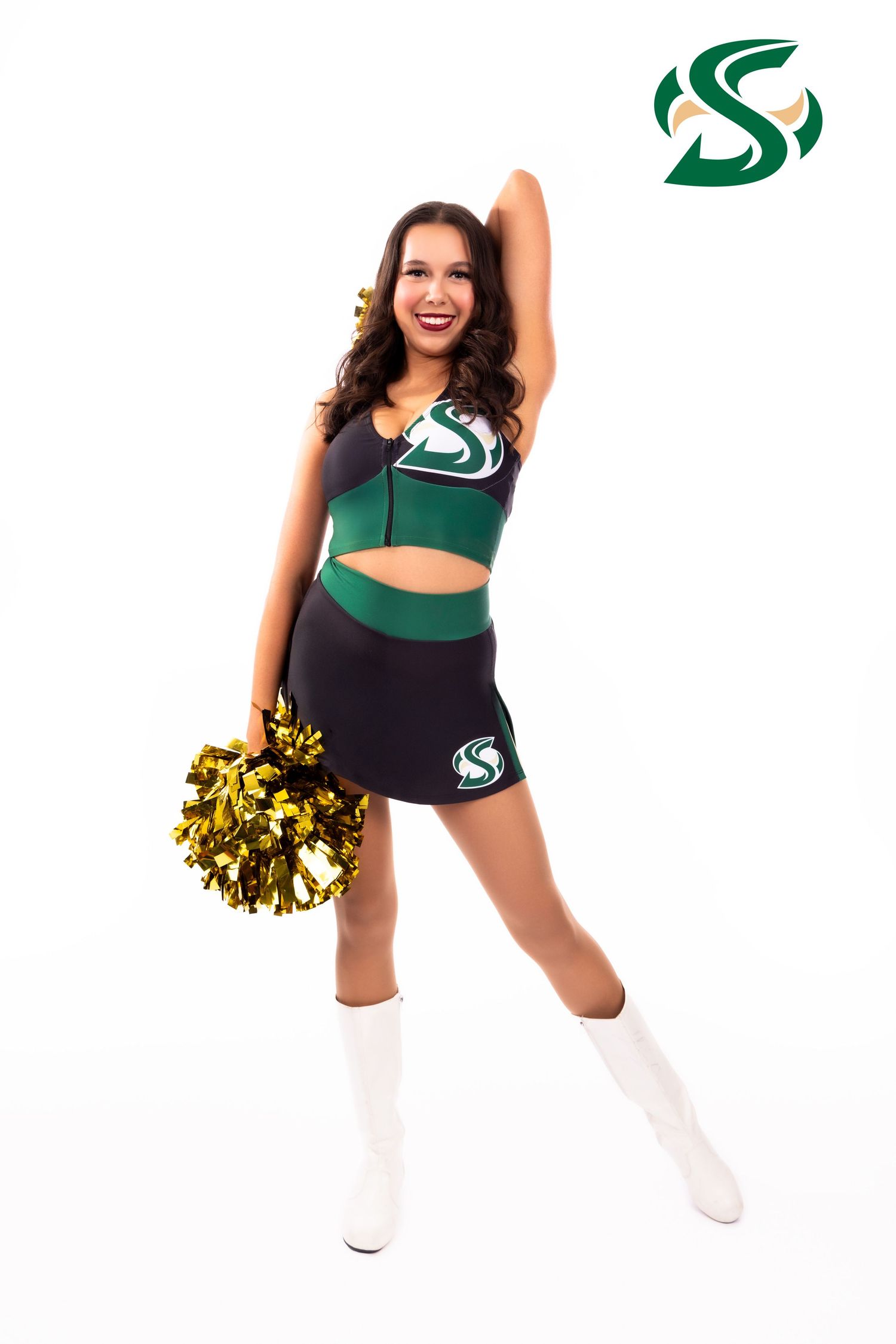 Cheerleader in green and black uniform with gold pom-pom poses energetically in front of white background.