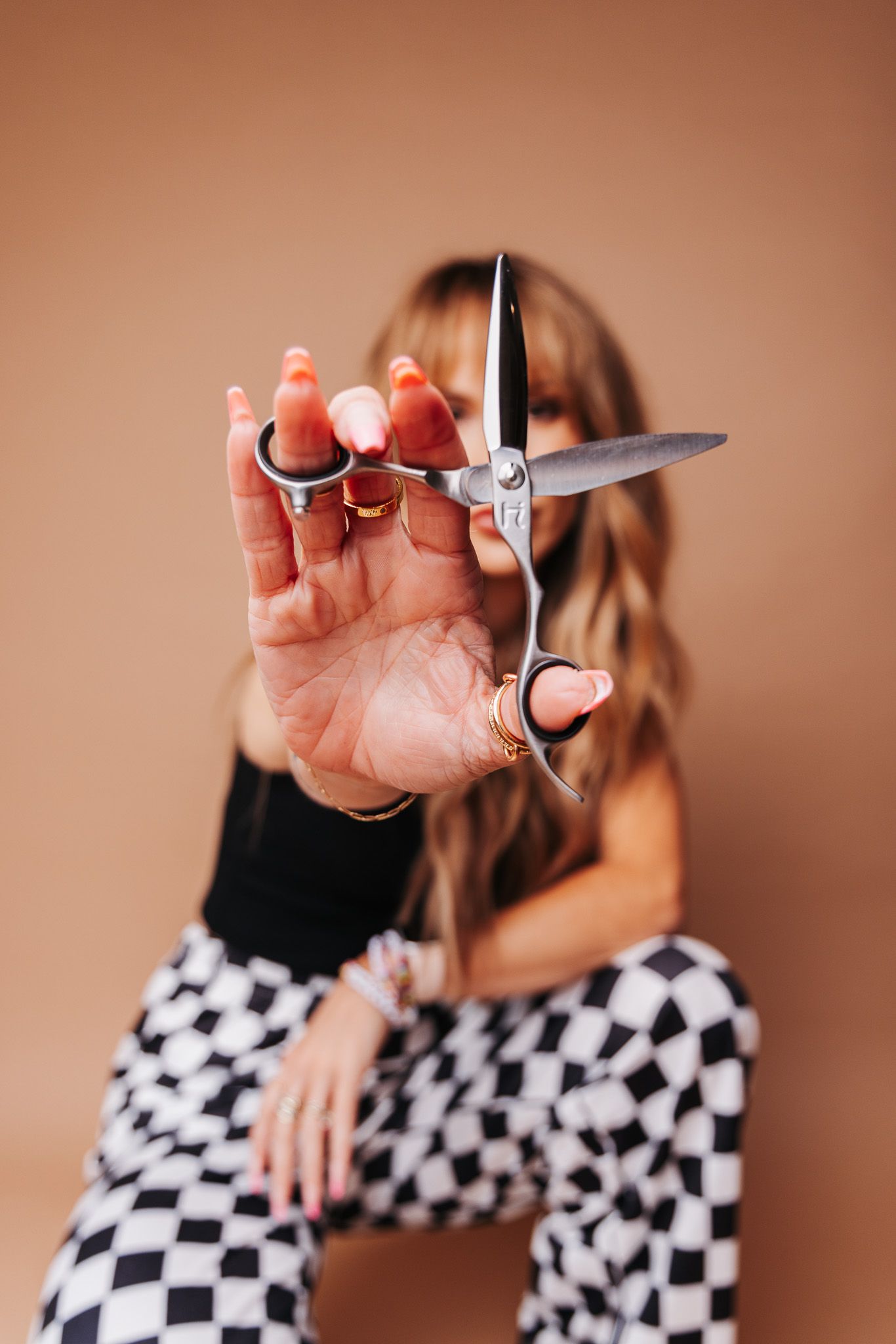 Hands holding hairdressing scissors shown against a black and white checkered pattern background.