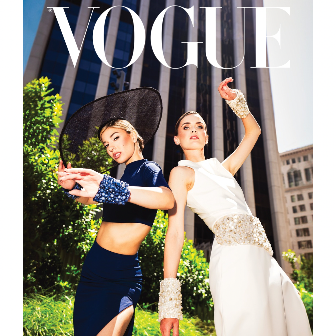 Two women in elegant dresses pose playfully during a wedding photoshoot in an urban setting.
