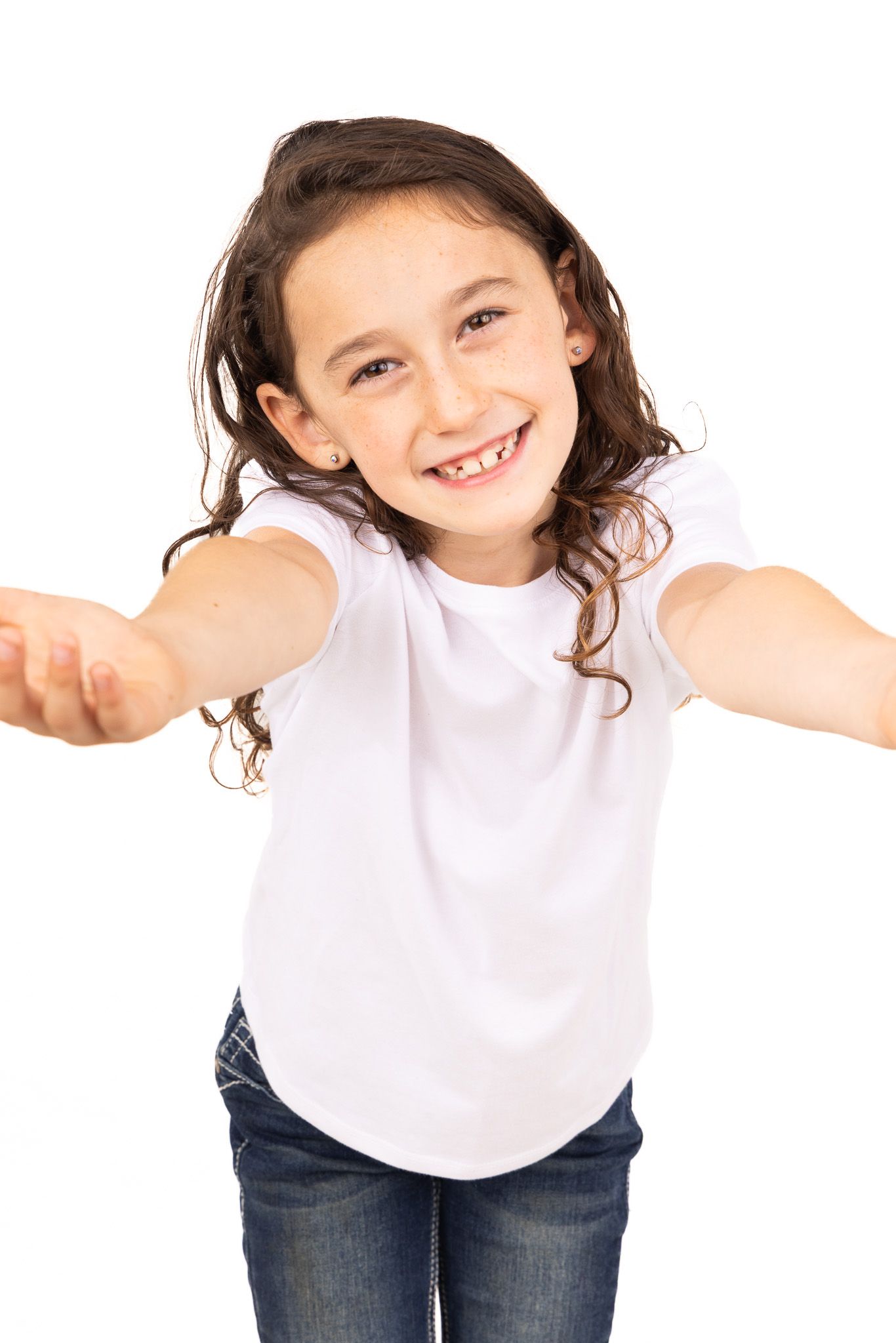 Child in white t-shirt and jeans stretches arms wide with joyful expression.
