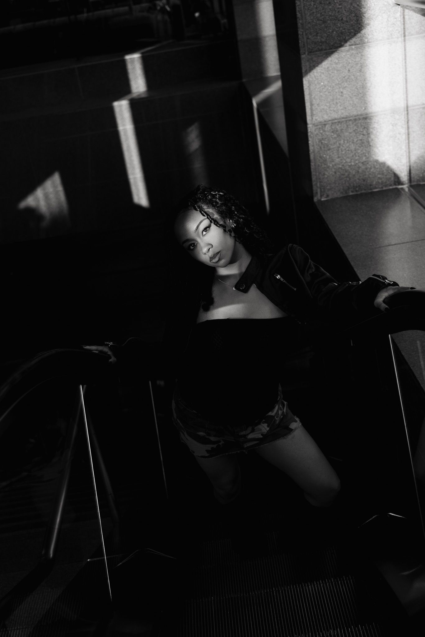 A dramatic black and white portrait showing a person in dark attire against shadowy architectural elements.