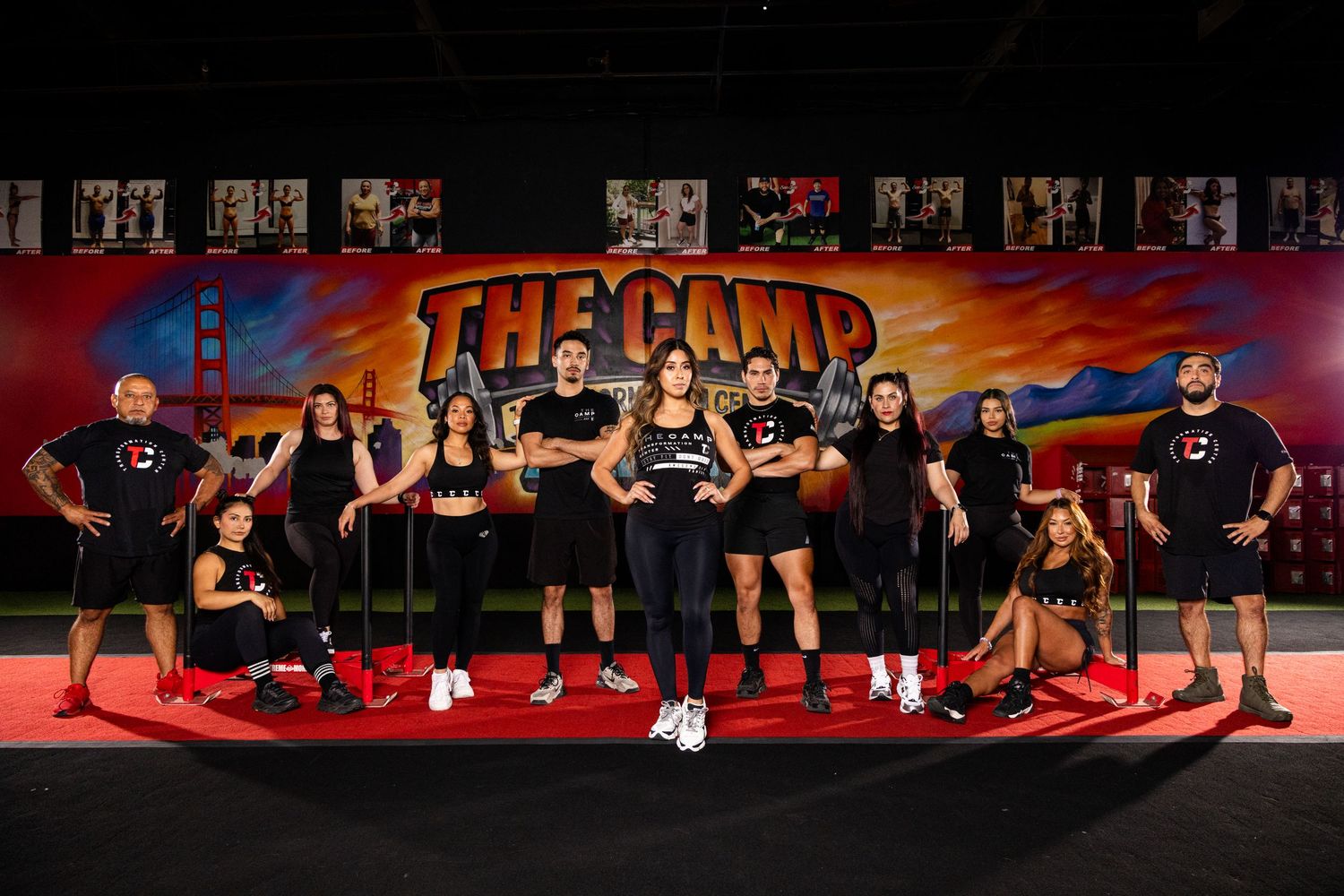 A group of fitness enthusiasts pose in workout gear against a colorful graffiti wall at a gym facility.