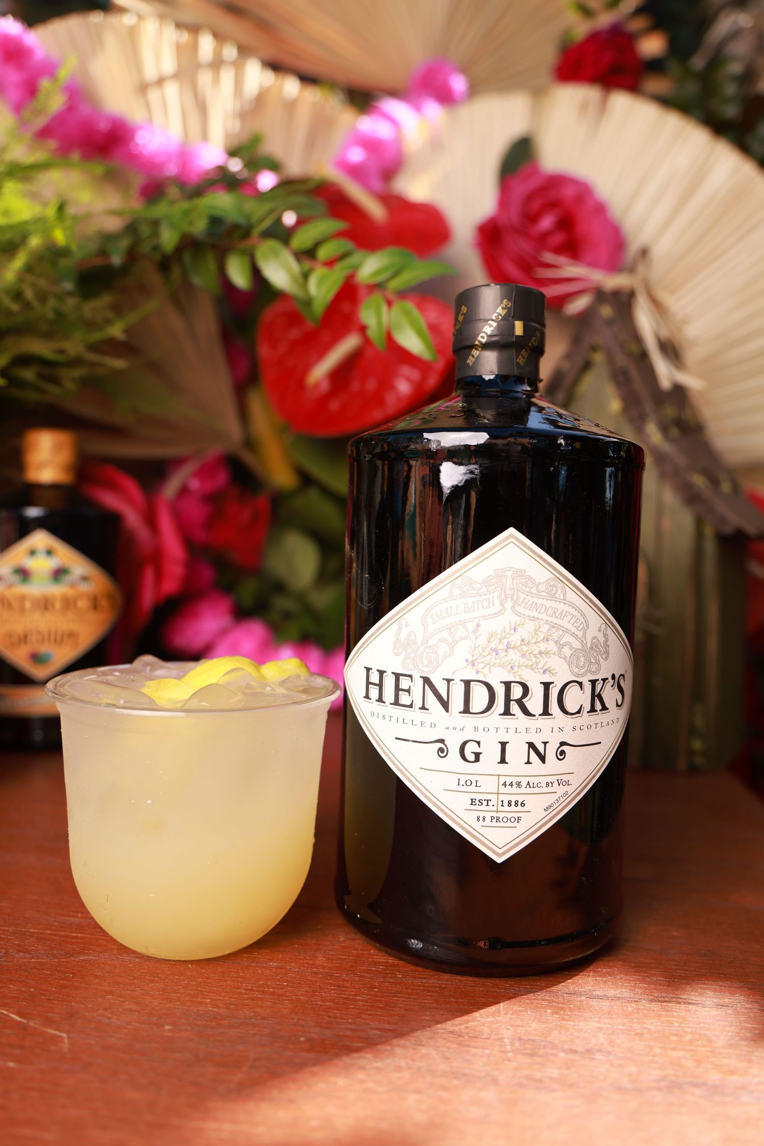 Hendricks gin bottle and cocktail glasses displayed on wooden bar with pink floral decorations.