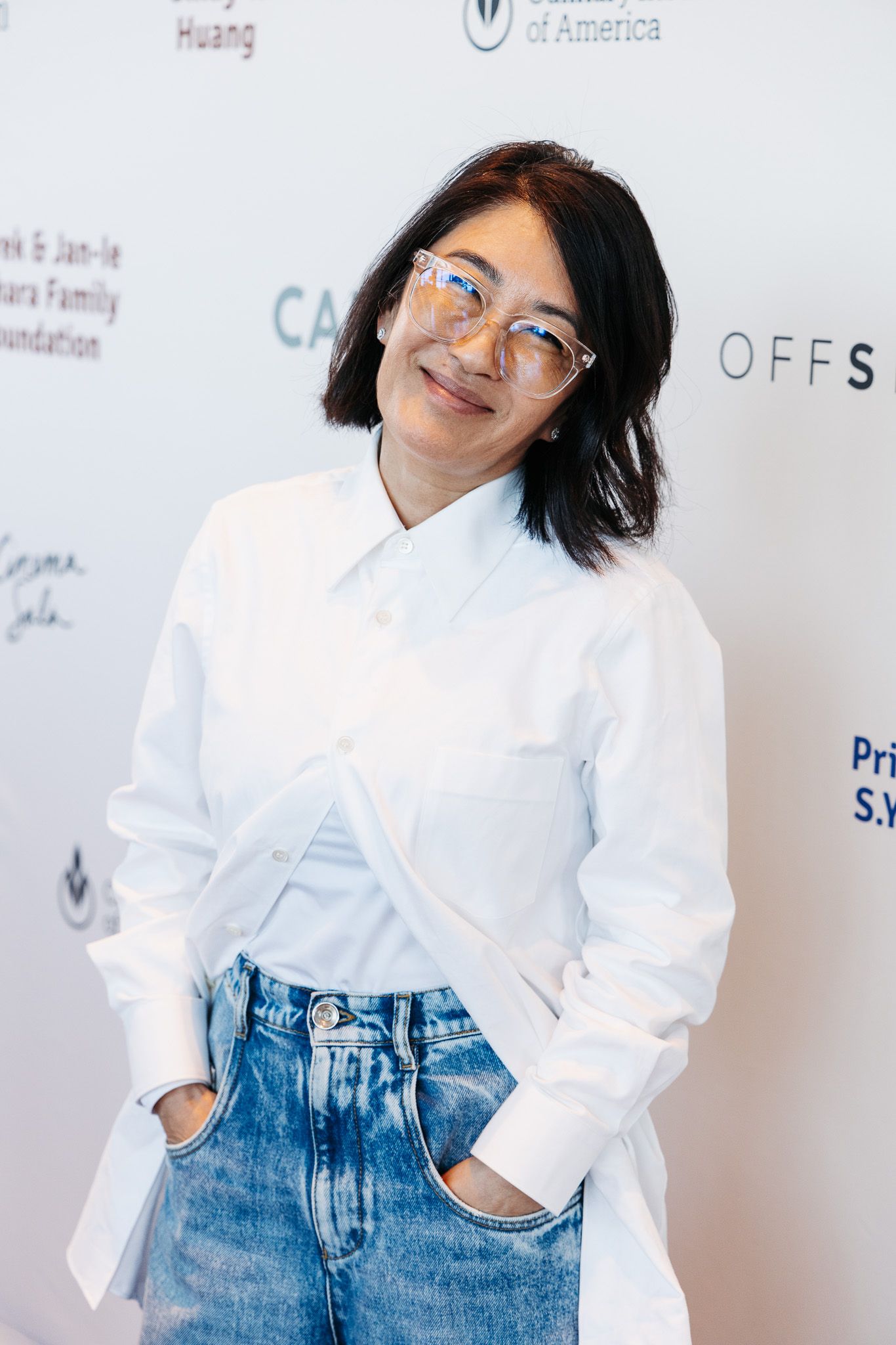 Person in white shirt and jeans poses against white backdrop at photo shoot.