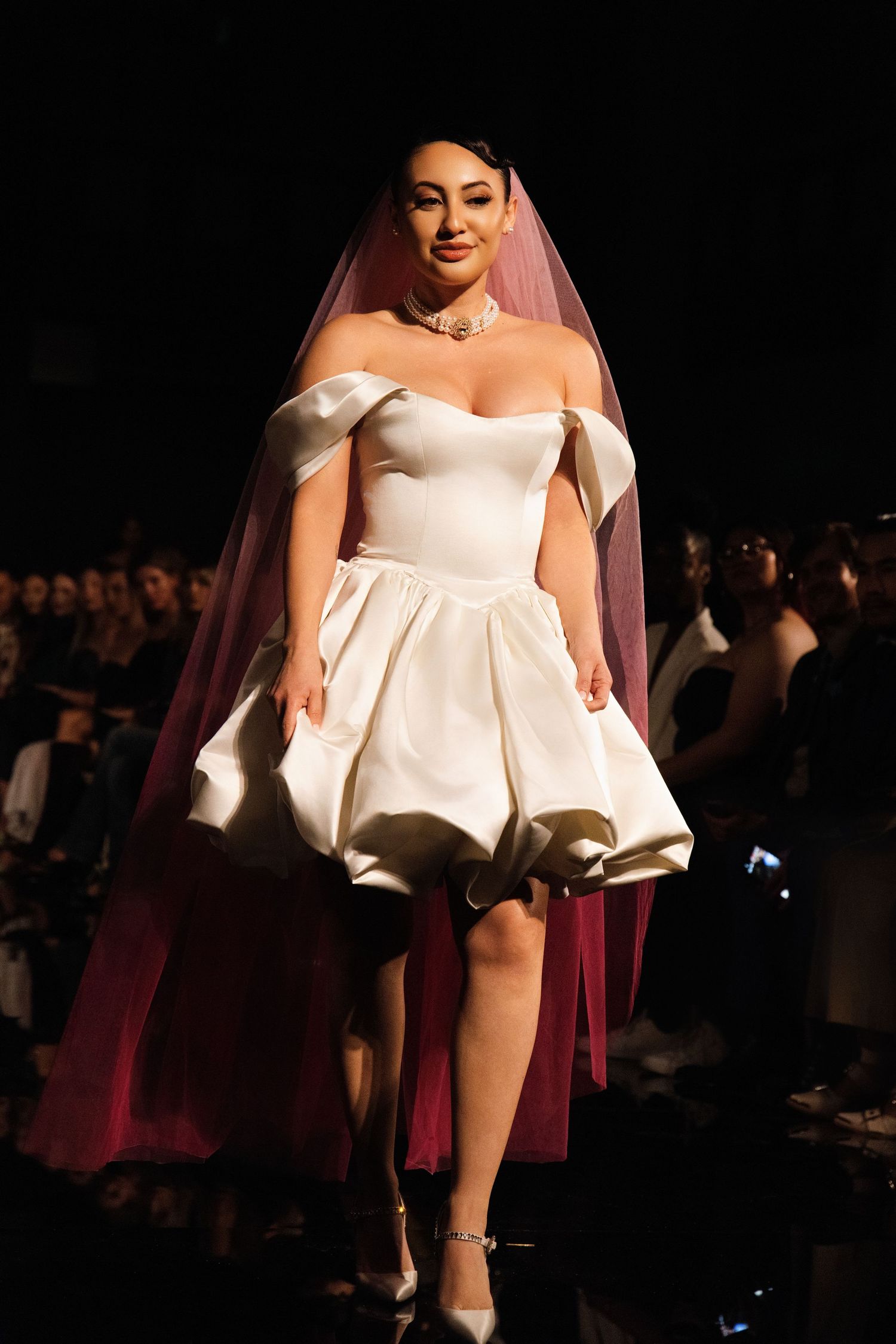 A model walks the runway in a short white strapless dress with architectural details during a fashion show.