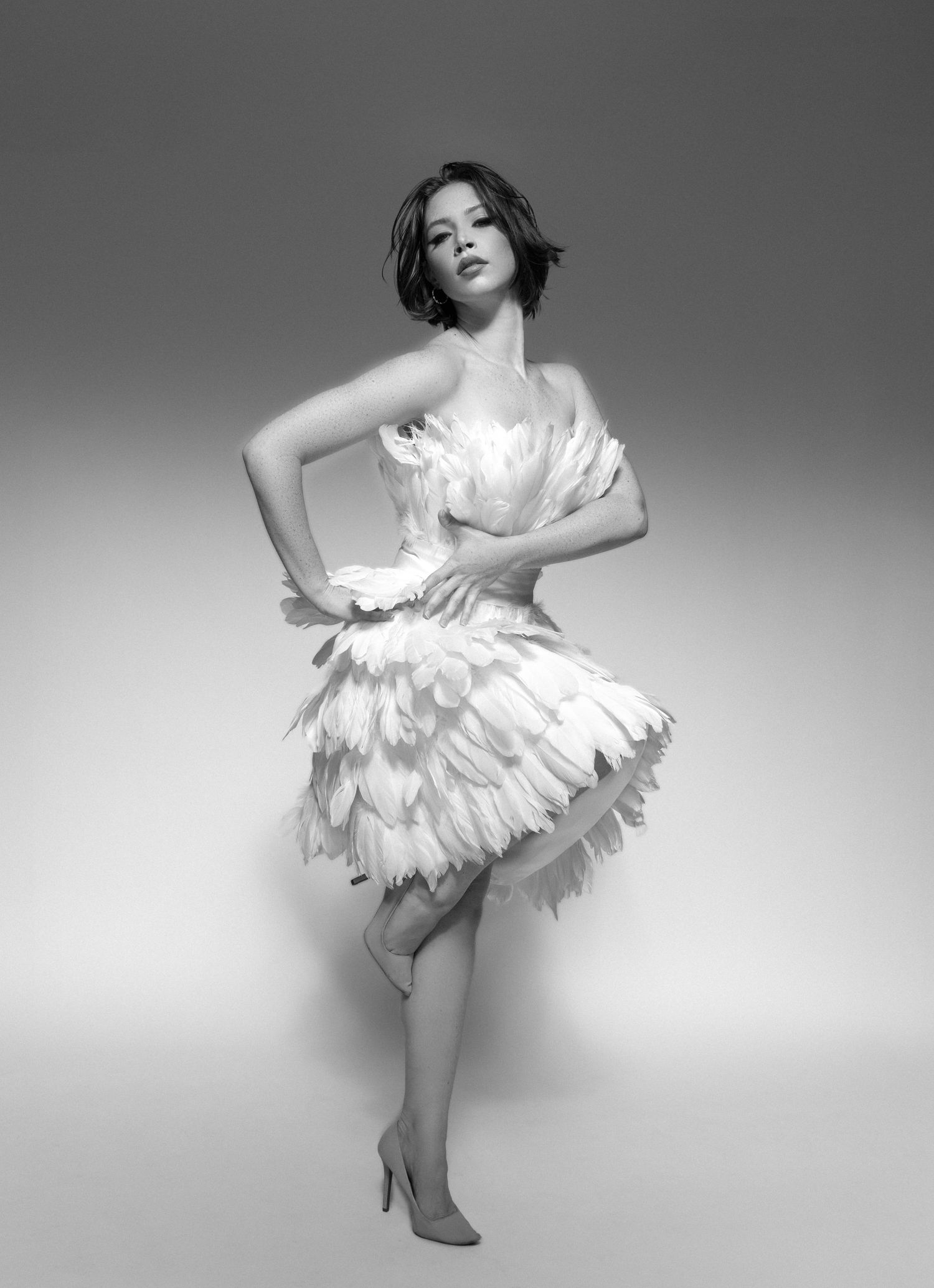 A graceful dancer in a white feathered dress performs a dynamic series of movements in black and white photography.