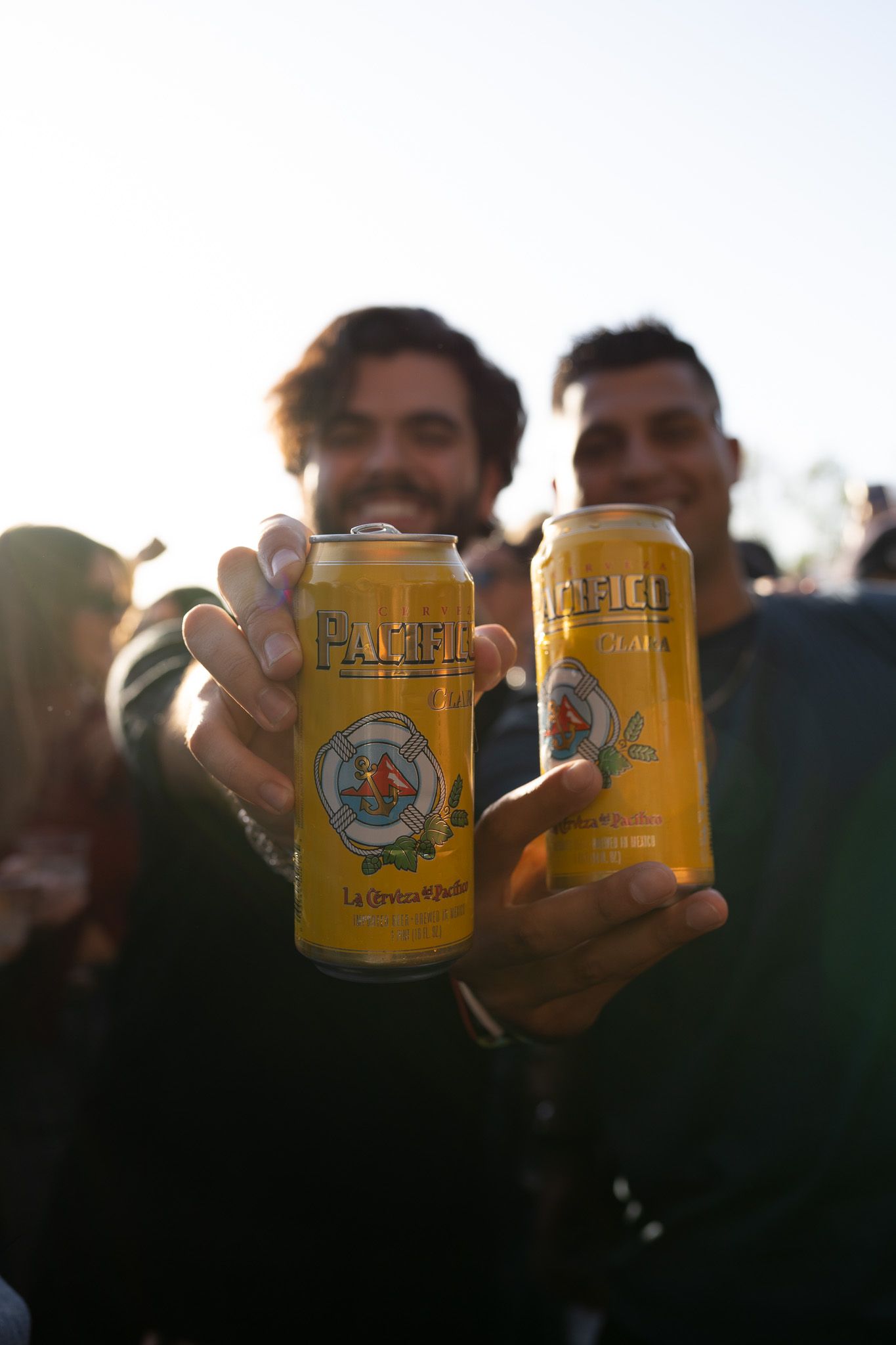 Friends toast with golden craft beer cans at sunset creating a celebratory outdoor gathering atmosphere.