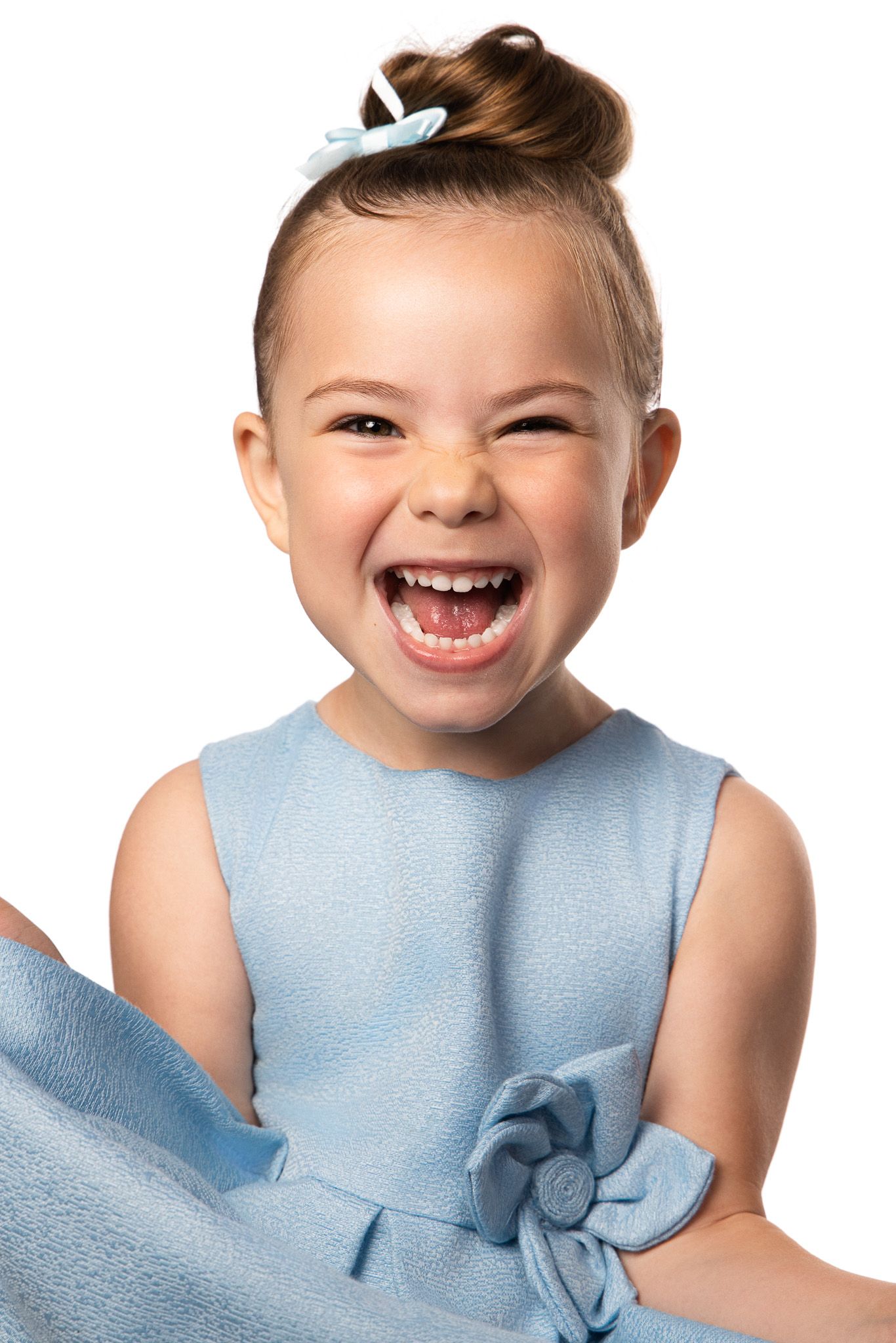 A joyful child wearing a light blue sleeveless dress with a floral detail laughs expressively against a white background.