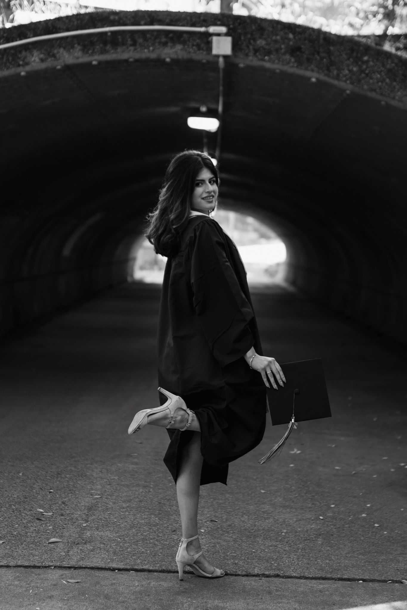 A black and white photo showing a person in a dark coat striking a playful pose in a tunnel.
