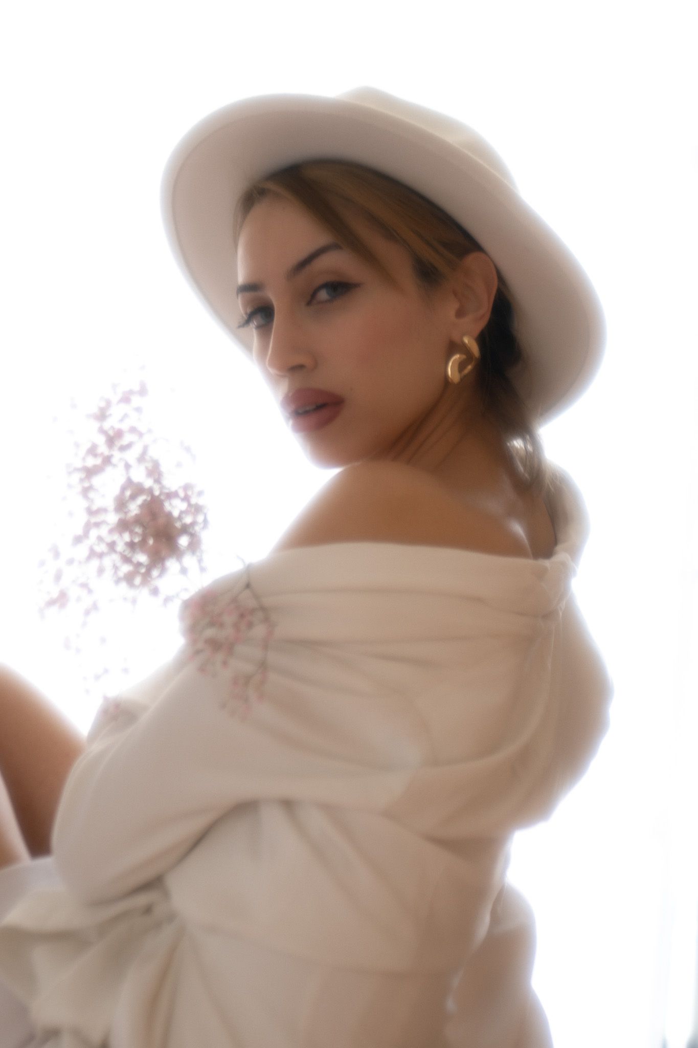 Figure wearing white winter fashion with cowboy hat and scarf poses in a bright artistic portrait series.