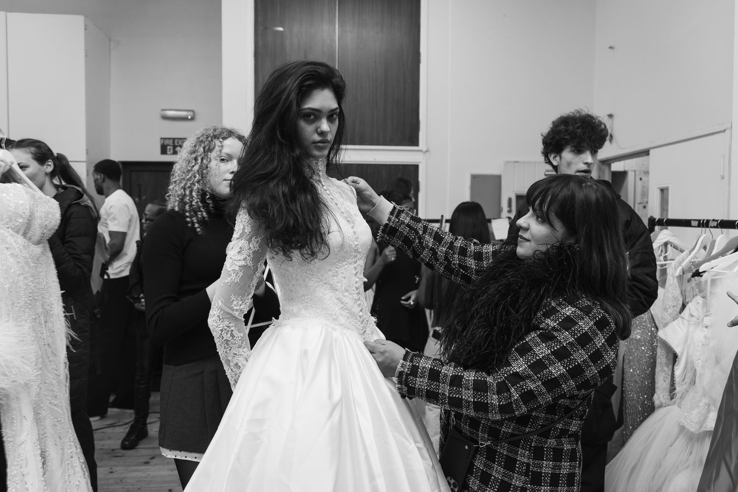 Black and white backstage photo of wedding dress fitting with seamstress making adjustments.