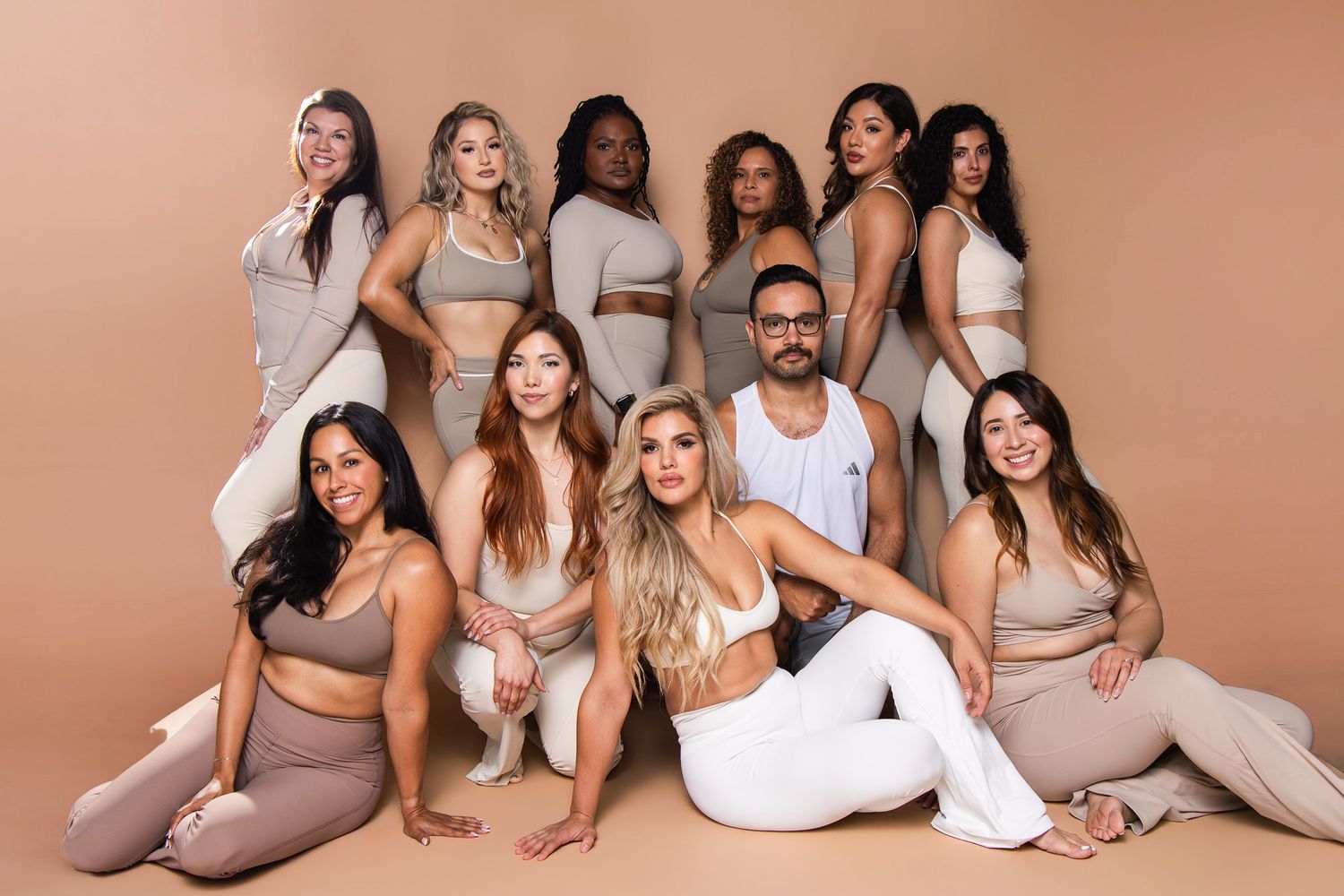 Diverse group of men and women pose together in neutral-toned activewear against a beige backdrop.